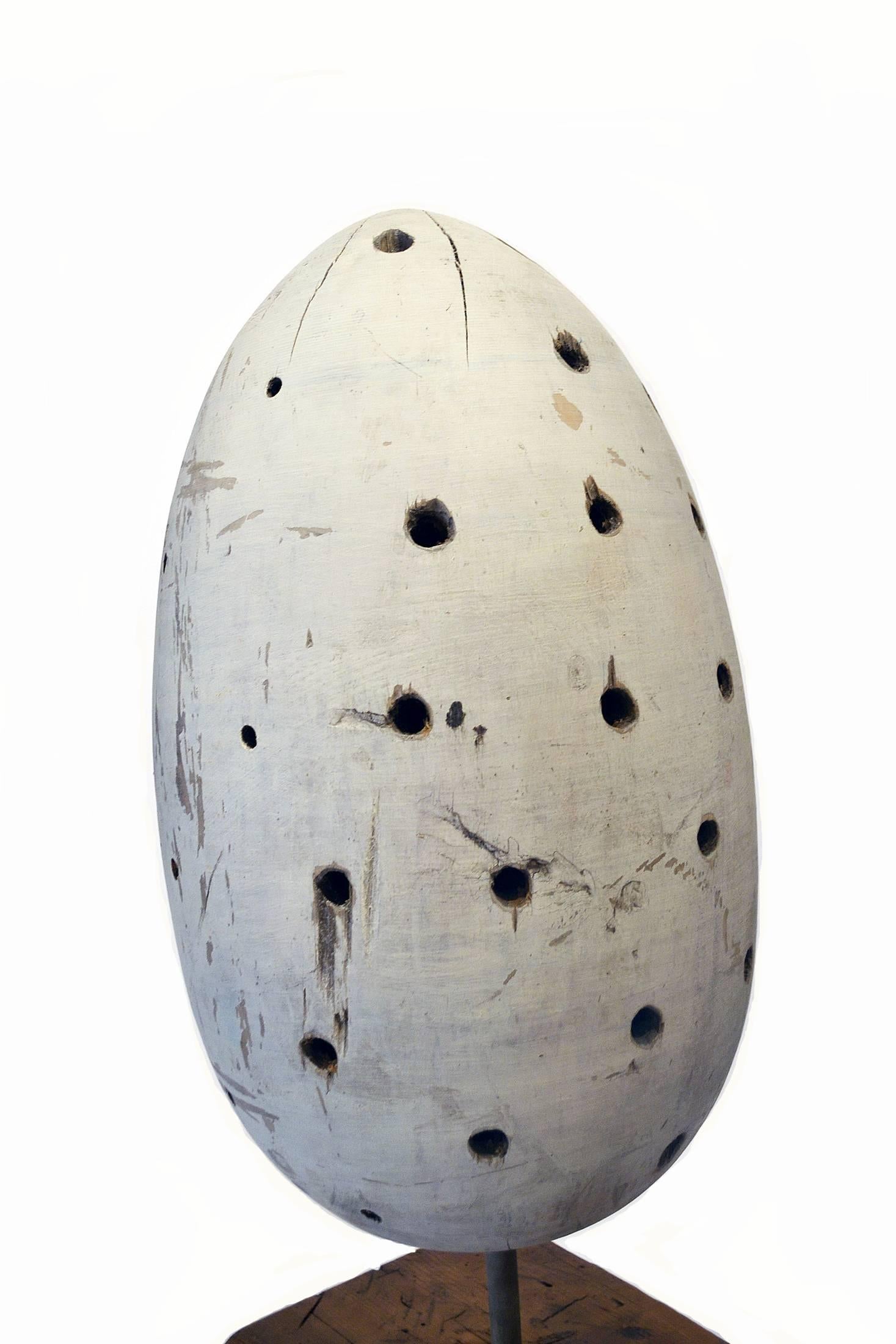 An exceptional carved wood sculpture in the form of a large egg, significantly dotted with holes and painted in a white wash. The sculpture sits on a metal rod that is mounted into a wood base. A striking work of art. Artist unknown.