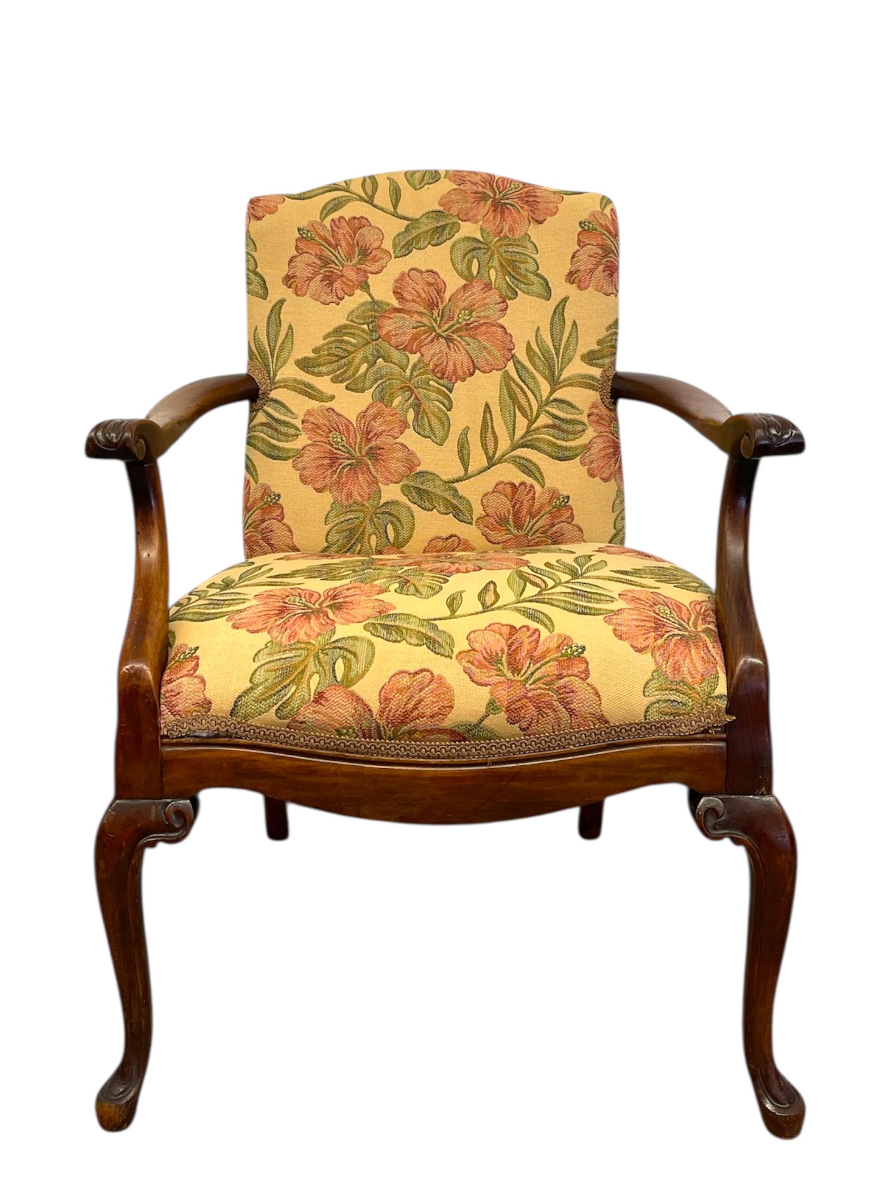  Gepolsterter Vintage-Sessel mit geschnitztem Holzgestell und geblümtem Stoff. Zu den Merkmalen gehören sanft gewölbte Arme, geschnitzte Blumendetails an den Handlehnen und klassische Cabriole-Beine. Die Silhouette lehnt sich an den traditionellen