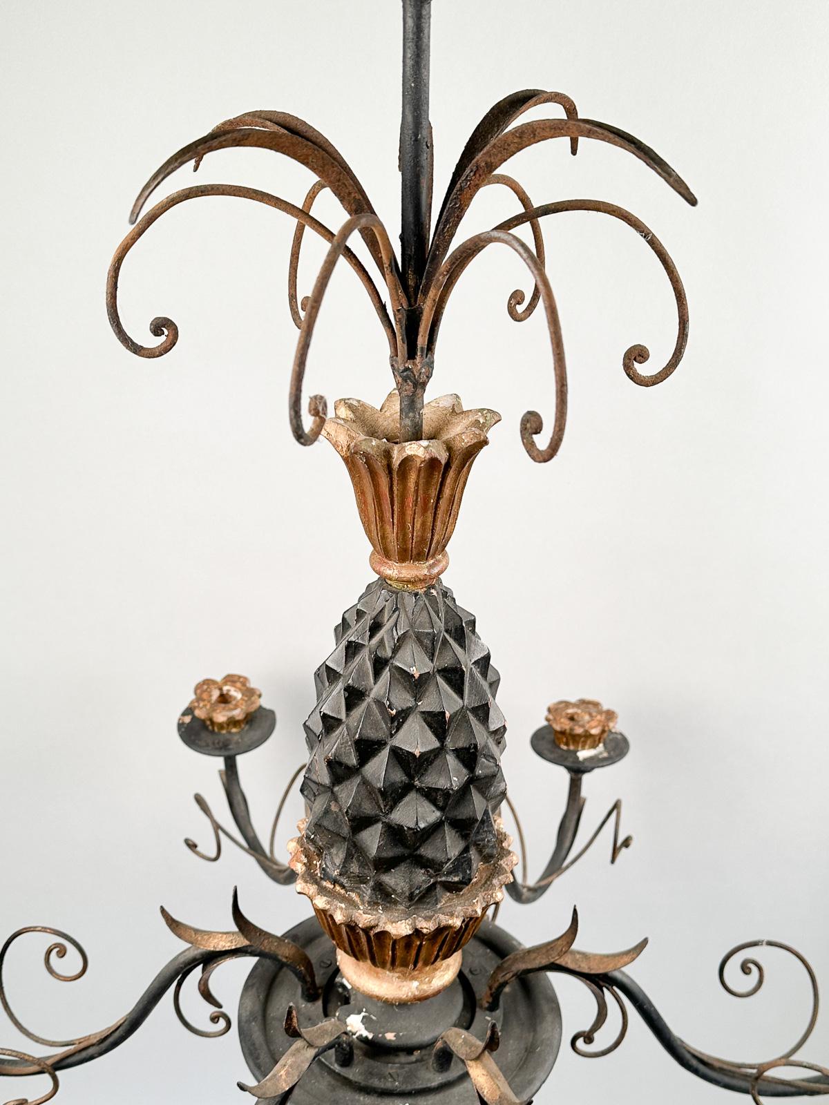 Insolito lampadario a candela ad ananas in legno intagliato, metà del XX secolo. Ananas in legno dipinto e dorato con foglie, che sorreggono sei 	bracci curvi in metallo dorato che sorreggono prese per candele a forma di petali e vaschette di
