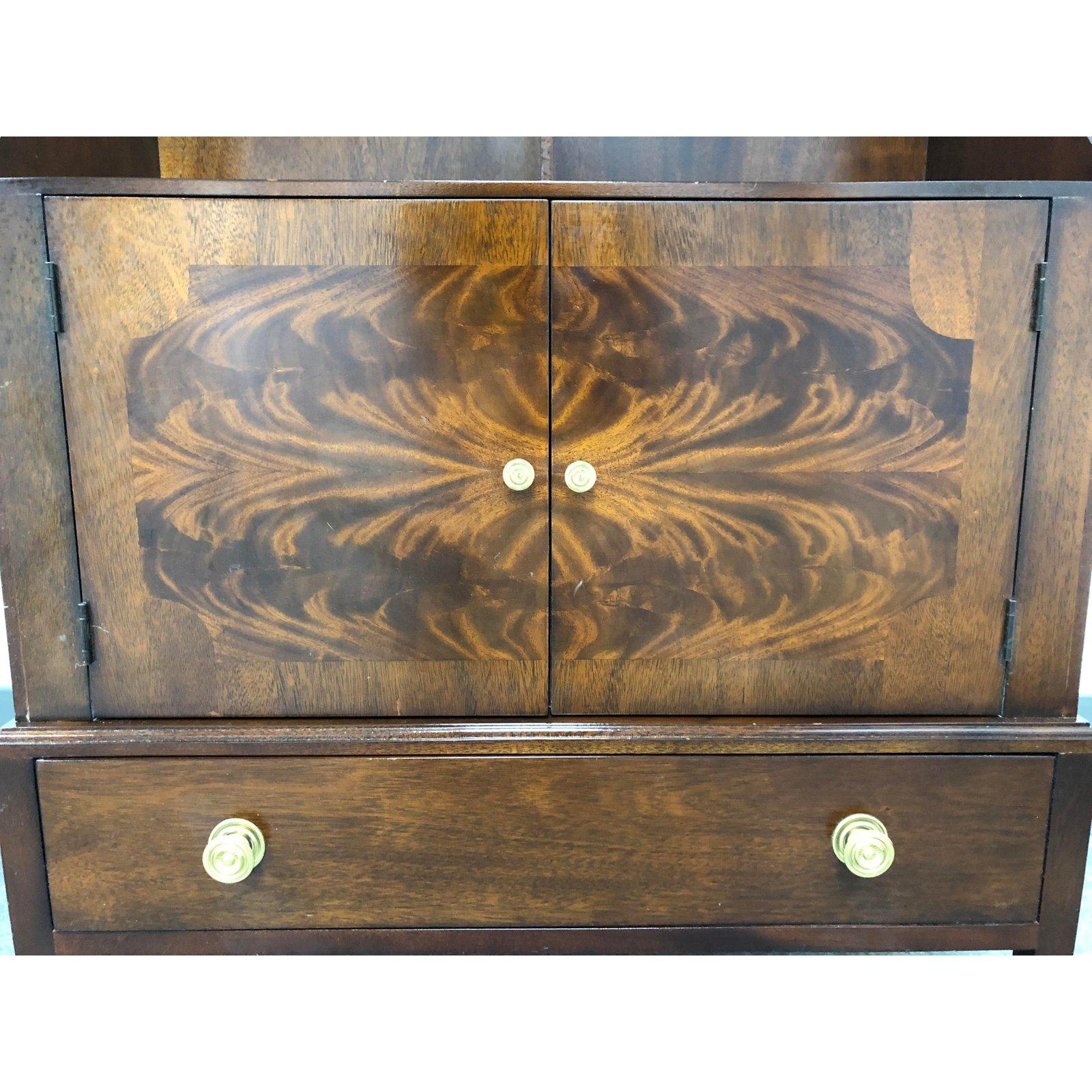 A vintage cabinet hutch. A one piece constructed of solid wood with dark finish veneers. The base consist of a single pullout drawer with two swing open doors to reveal hidden storage. The frame has a cascaded wood trim. Towards the top has five