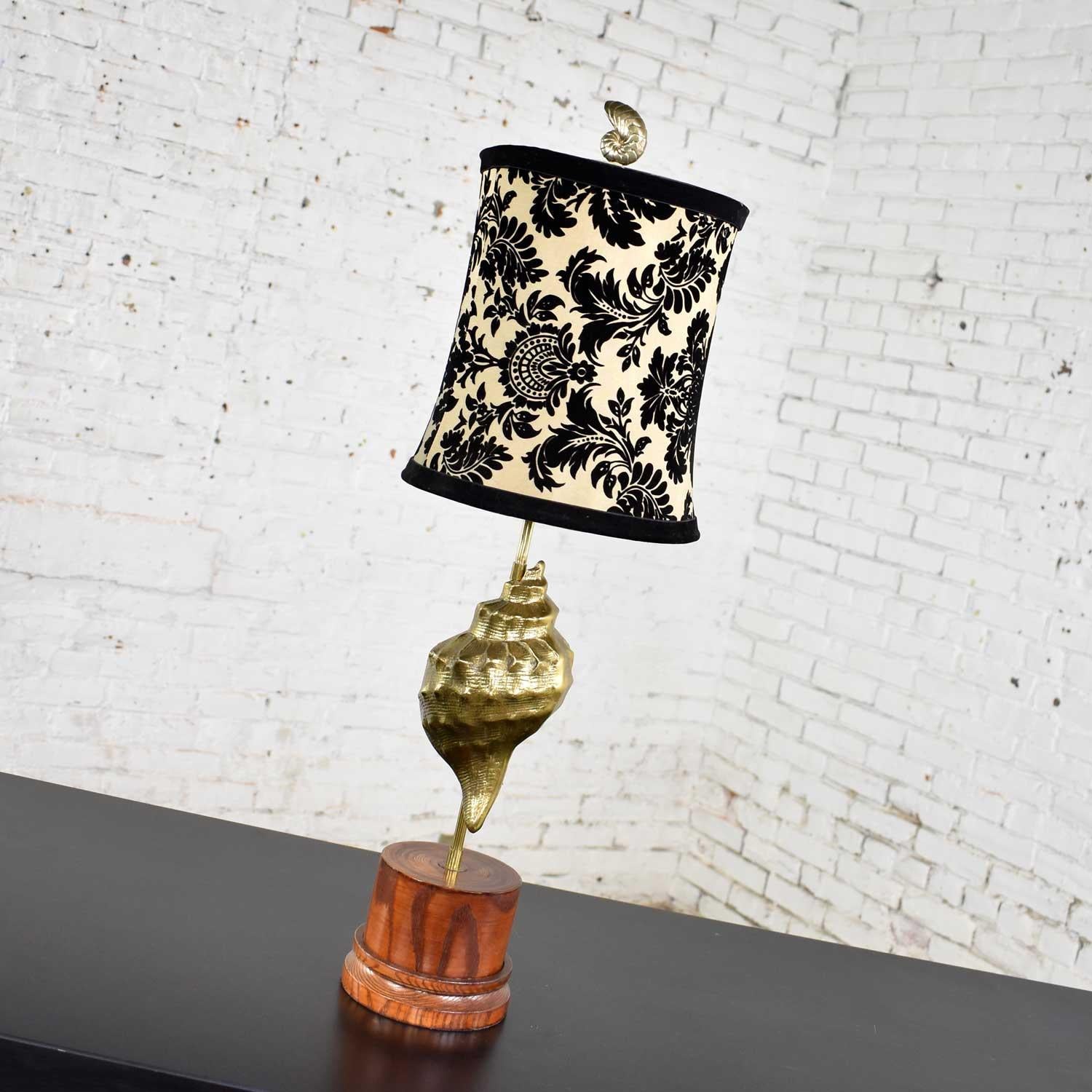 Awesome vintage cast brass conch shell table lamp on a turned wood base. It is adorned with a relatively new black velvet and taffeta lamp shade. It is in wonderful vintage condition with age appropriate wear to both lamp and shade. Please see