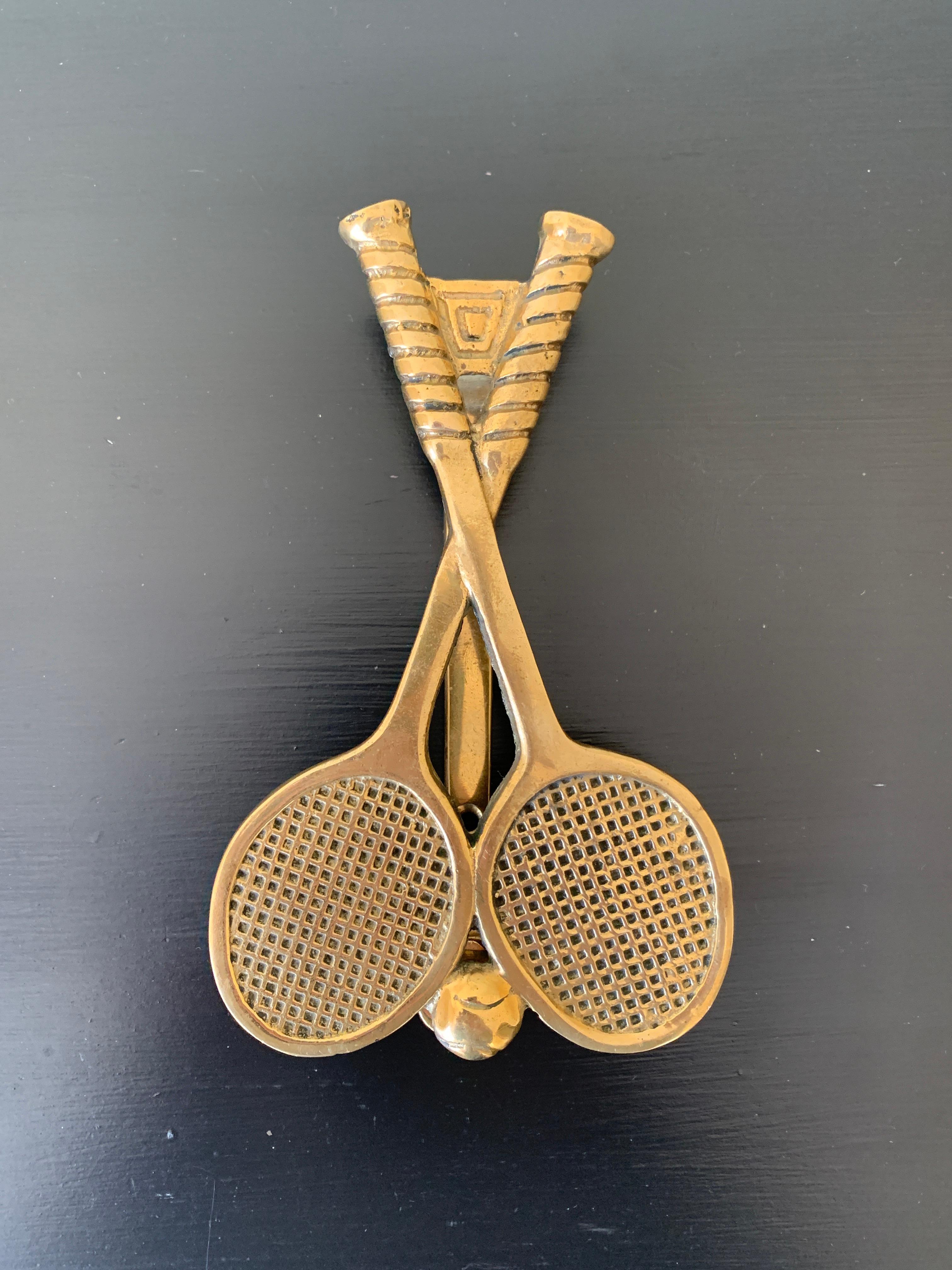 A beautiful cast brass door knocker in the form of two tennis rackets and a tennis ball.

USA, Mid-20th Century

Measures: 4