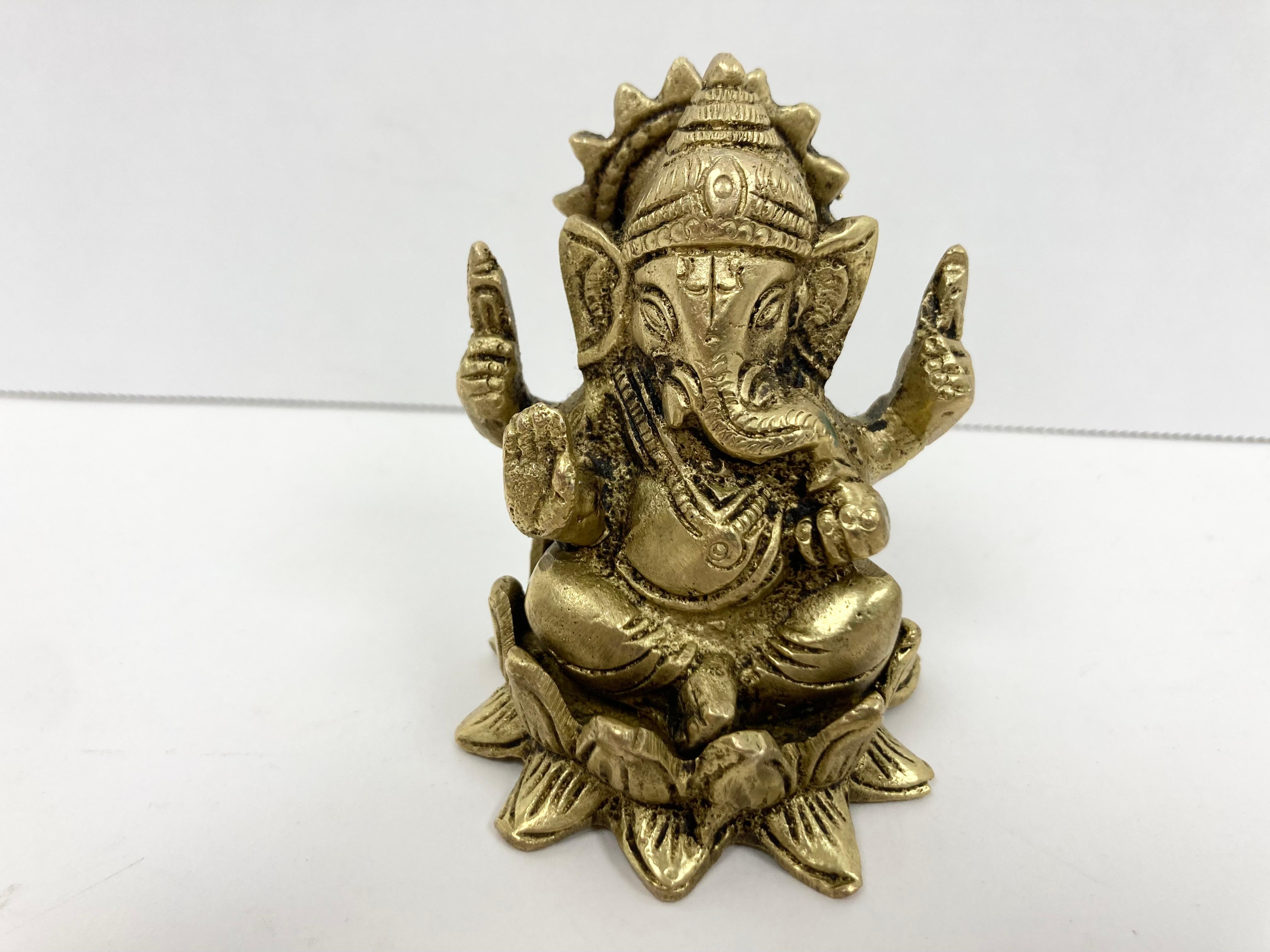 Eine aus Messing gegossene Andachtsskulptur von Ganesha. Auf einem Lotusthron sitzend, hält er in traditioneller Haltung die Symbole seiner Gottheit als Herr der Künste und Wissenschaften und Zerstörer von Hindernissen in die Höhe. In das gegossene