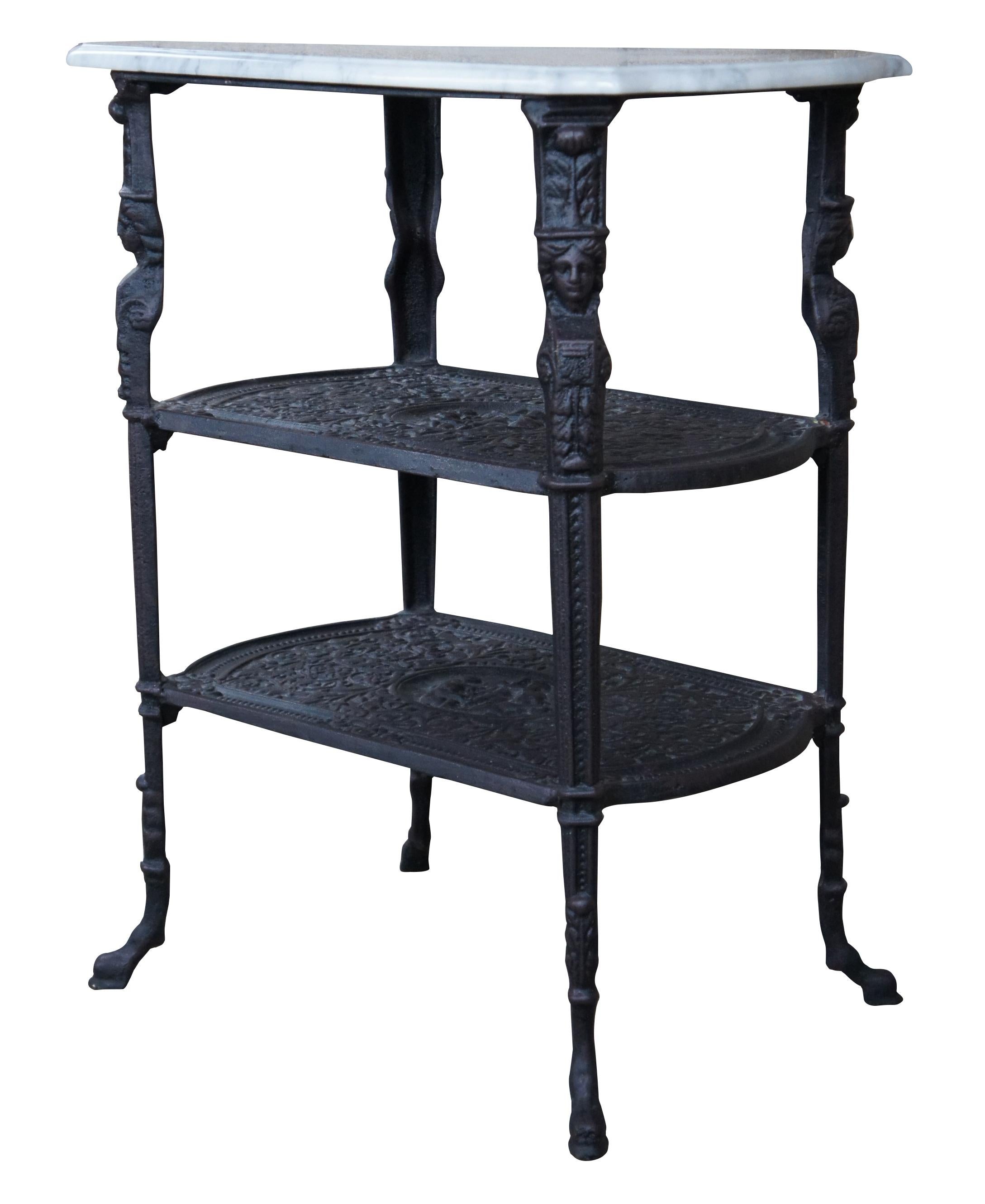 Vintage cast iron and marble top parlor side table or plant stand featuring three tiers with Egyptian Caryatid columns, cameos of cherubs and hooved feat. Very heavy. Measure: 29
