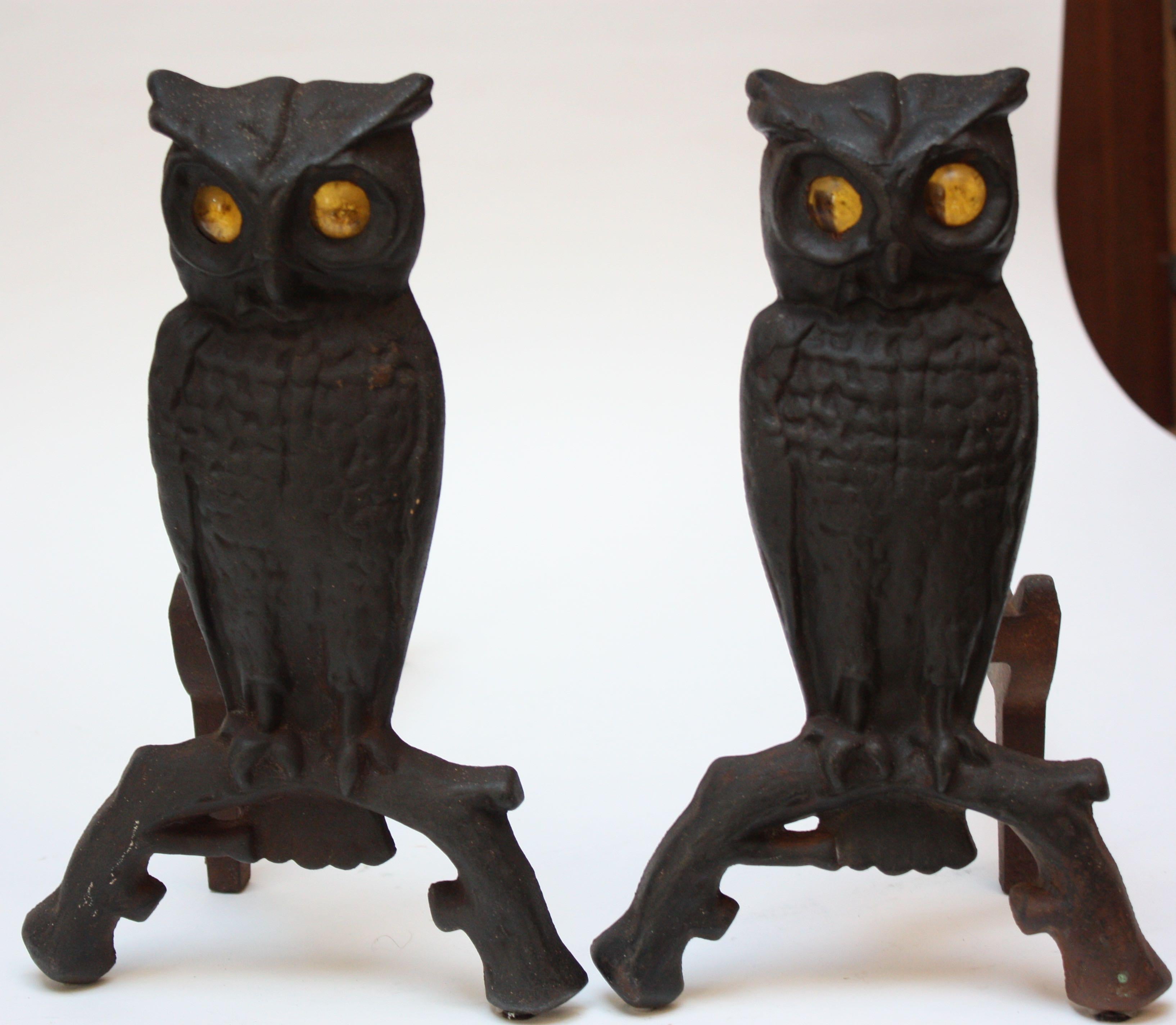 This pair of early 20th century andirons is composed of cast iron owls on arched branch uprights fitted to billet bars. The glass amber eyes, which glow when placed in front of a fire, are nicely contrasted by the black cast iron. All the hardware