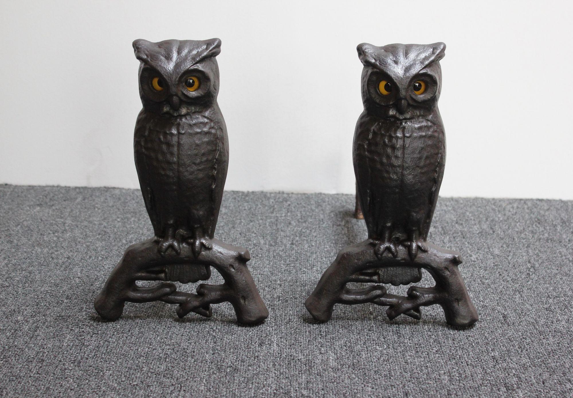 Pair of andirons (circa 1930s, USA) composed of cast iron owls on arched branch uprights fitted to billet bars. The glass amber eyes with black pupils, which glow when placed in front of a fire, are nicely contrasted by the dark brown cast