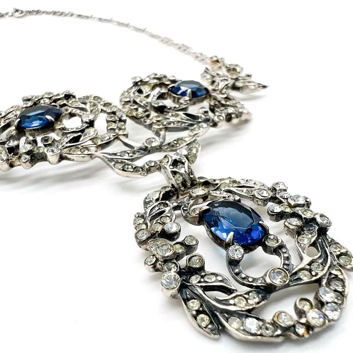 A Sterling Silver Vintage Castlecliff Sapphire Paste Necklace inspired by Renaissance jewellery styles. The delicate sterling silver scroll and leaf motif setting making the perfect backdrop for the tiny clear chaton pastes and trio of deep sapphire