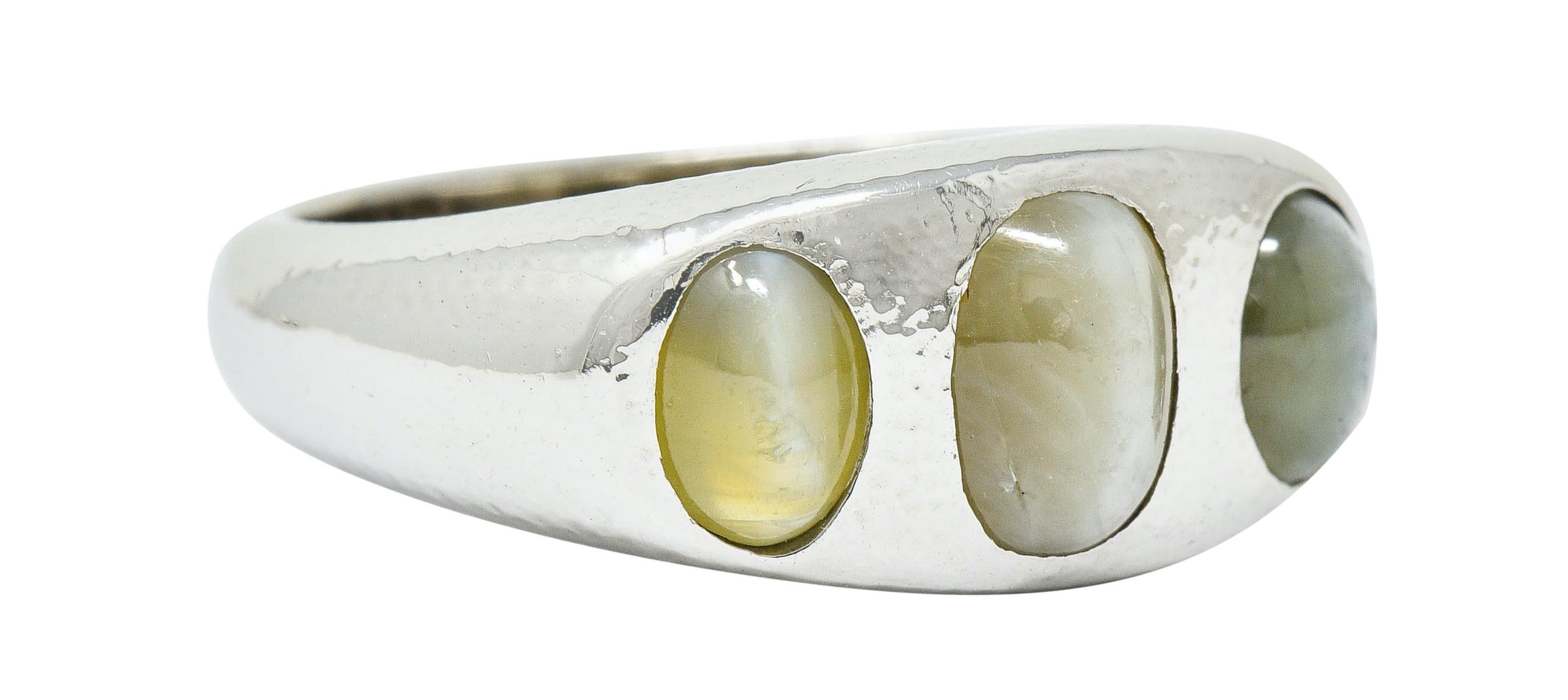 Hammered band ring centers three flush set cat's eye chrysoberyl

Translucent with light green color to yellowish-green

All exhibit a crisp chatoyant white line

Stamped 18K for 18 karat gold

Ring Size: 6 & sizable

Measures: 8.7 mm wide and sits