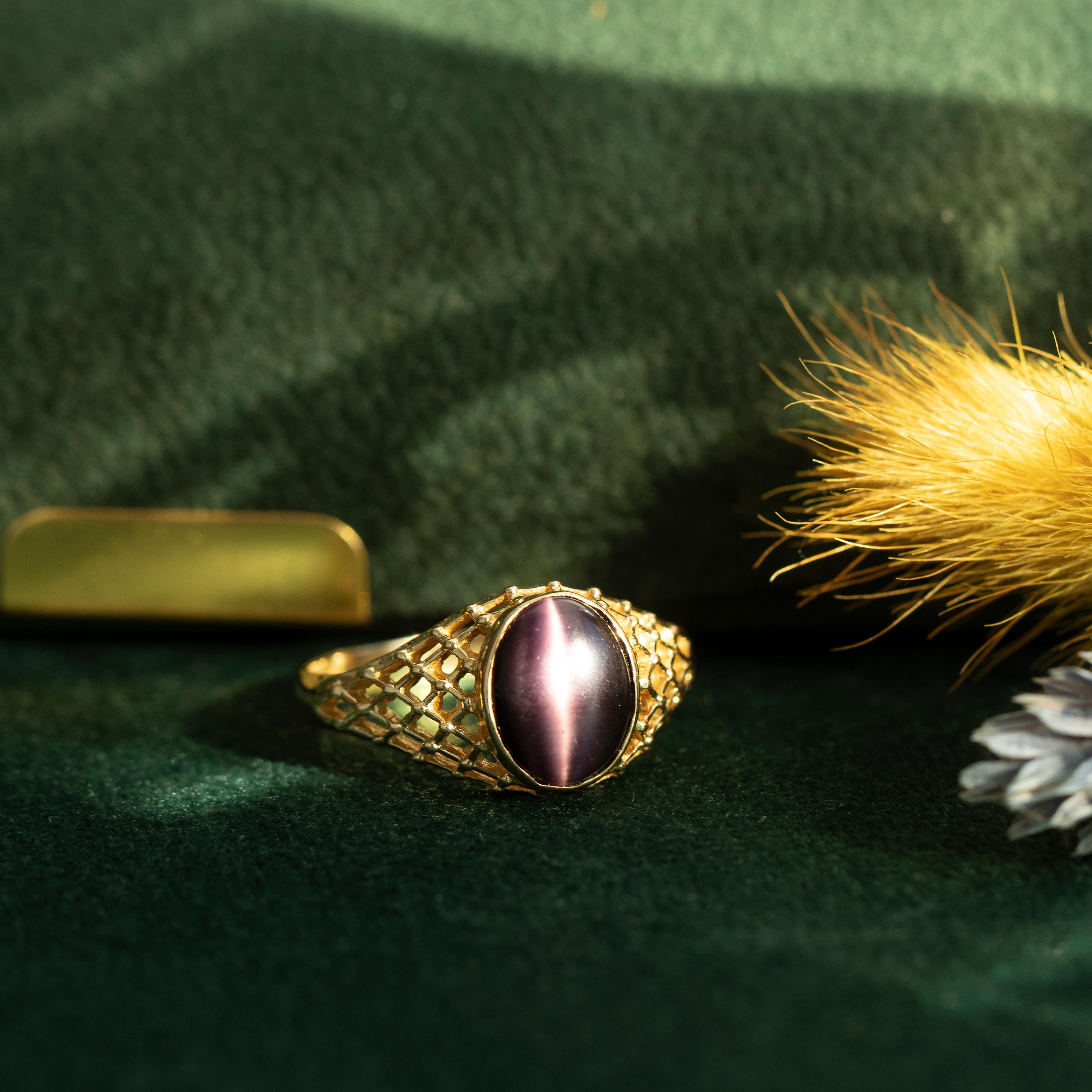 Ein aus 18-karätigem Edelgold gefertigtes Gitter umschließt einen violetten Glas-Edelstein. Chatoyancy ist ein Edelsteinphänomen, bei dem ein helles Lichtband auf der Oberfläche eines Edelsteins erscheint. Es ist auch als Katzenauge bekannt und wird