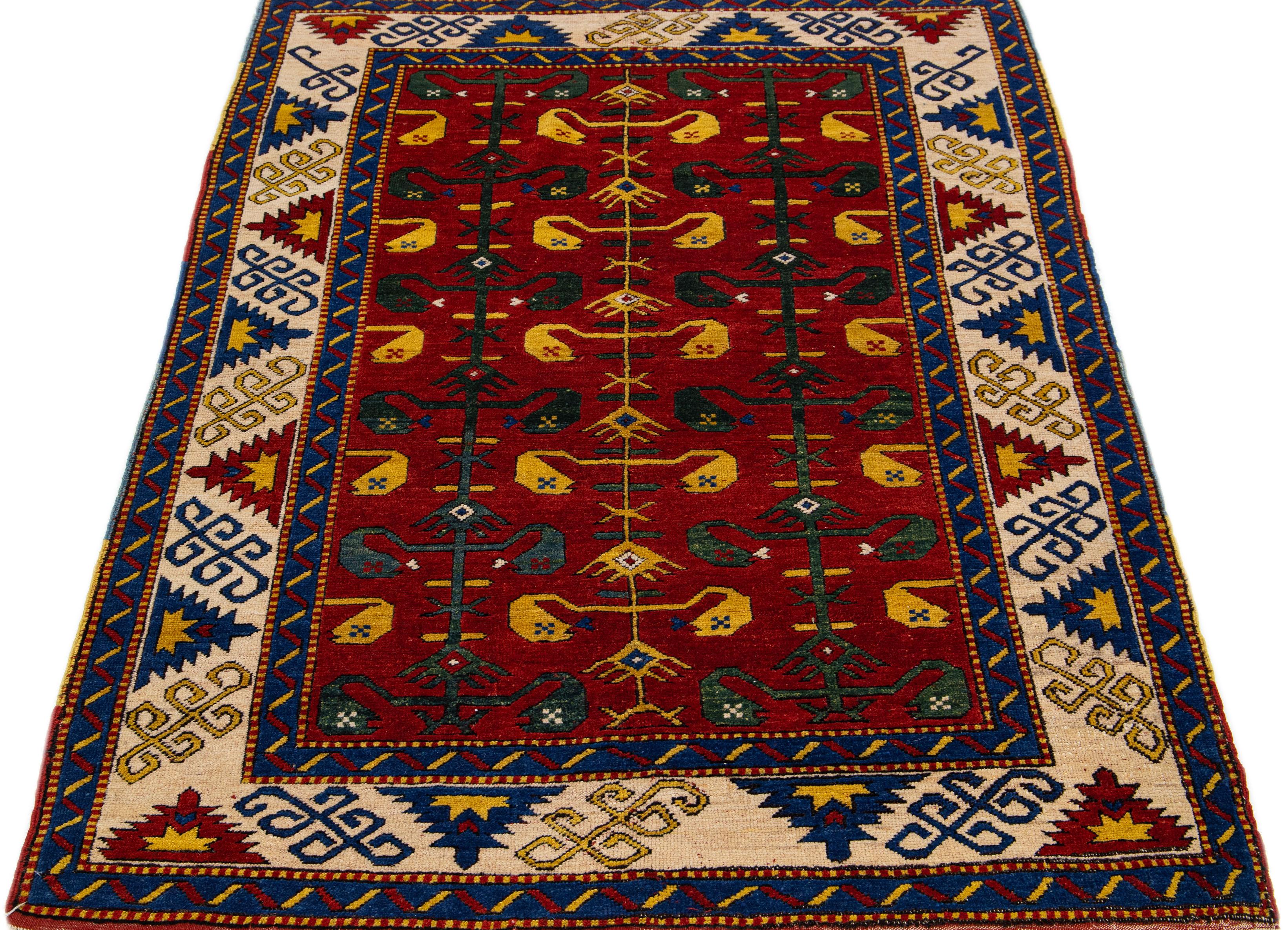 This Kazak wool rug is meticulously crafted by hand. The rug boasts a rich red palette, adorned with delicate embellishments in varying shades of yellow, green, blue, and beige, showcasing an intricate geometric pattern that covers the entirety of