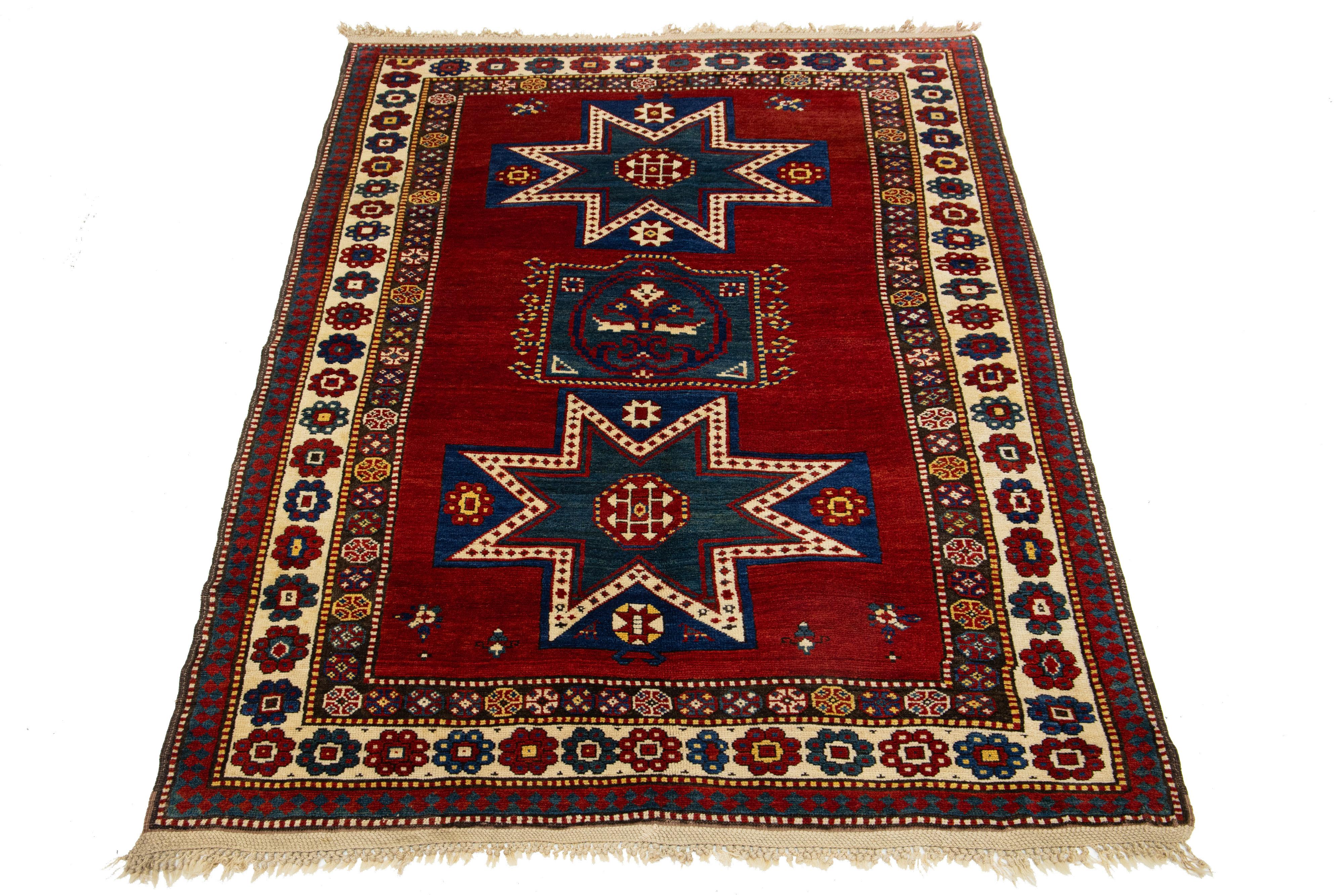Dieser Teppich aus kasachischer Wolle wird in sorgfältiger Handarbeit hergestellt und zeichnet sich durch eine satte rote Farbpalette aus, die mit zarten Verzierungen in Gelb-, Grün-, Blau- und Beigetönen geschmückt ist. Der Teppich weist außerdem