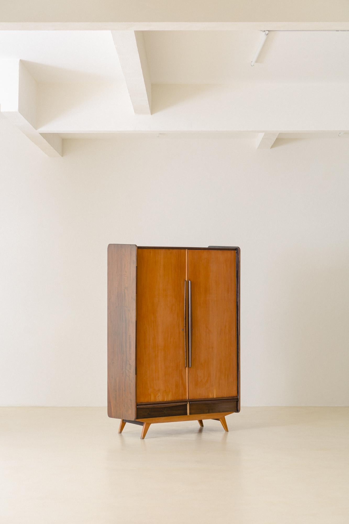 This charming wardrobe belongs to Móveis Cimo's furniture manufactured during the 1960s. The piece is composed of two types of Brazilian wood: the doors and feet are made of golden Caviuna, and the sides, drawers, and handlers are made of a dark