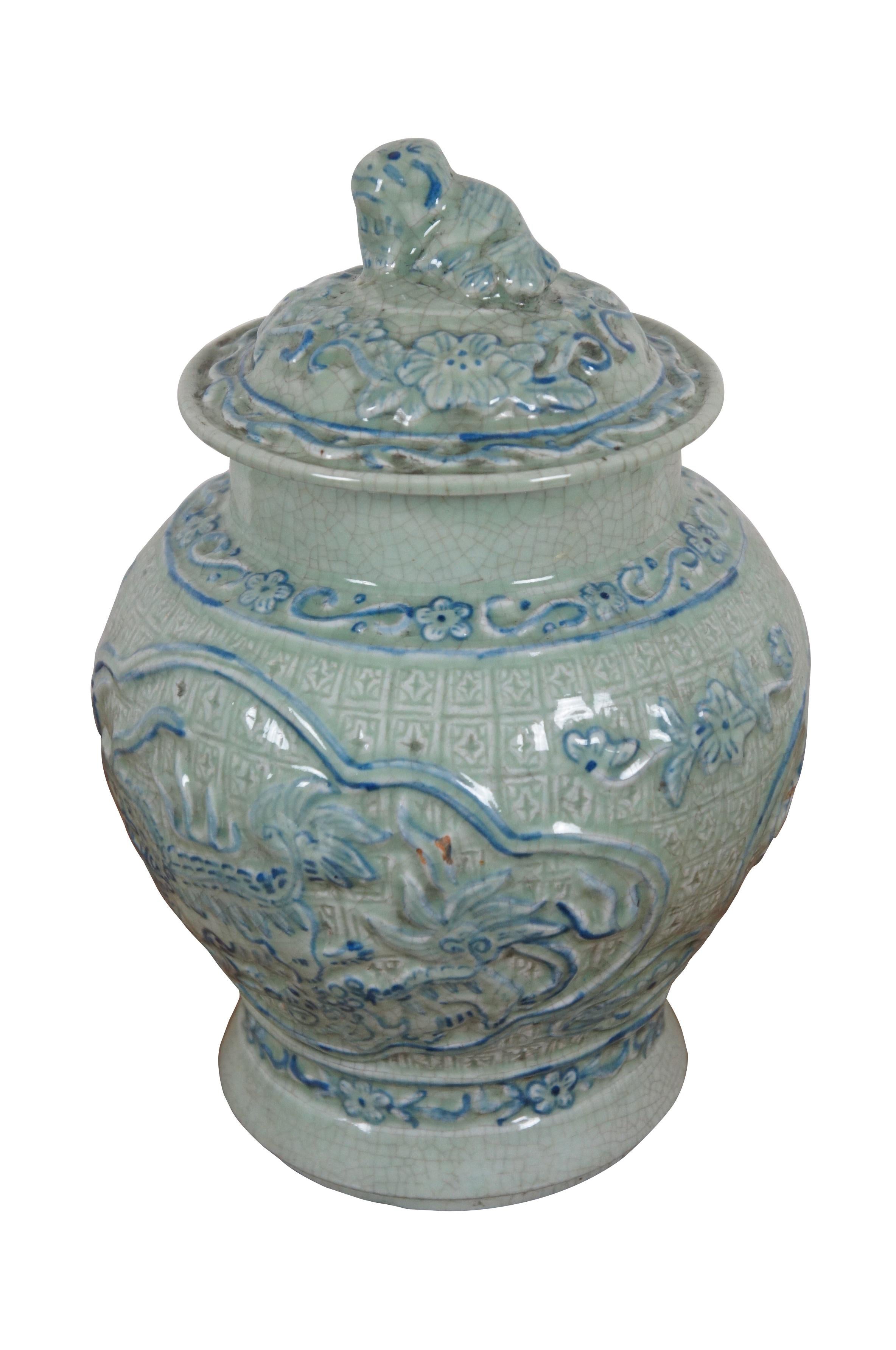 Chinese ginger jar / lidded urn crafted of pale celadon green, crackle glaze porcelain with blue painted details, intricately molded with floral patterns and guardian lions / fu dogs.

Dimensions:
7.75