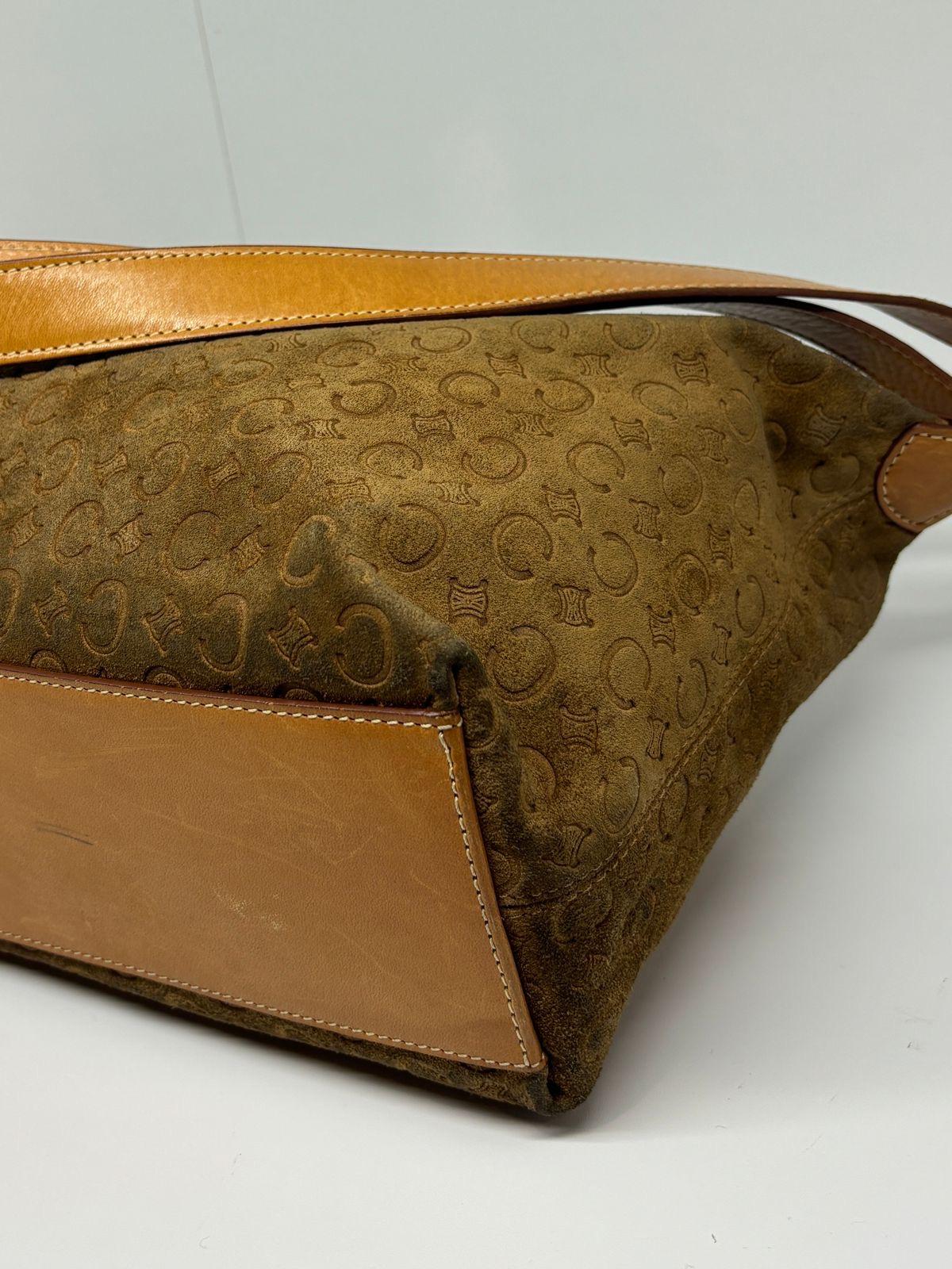 Item shows slight signs of wear and storage throughout, with marks on the suede surface. Visible dark rubbing marks on the corners. The leather handle shows darkening on the side that is in contact with the metal hardware. Item comes as is.
