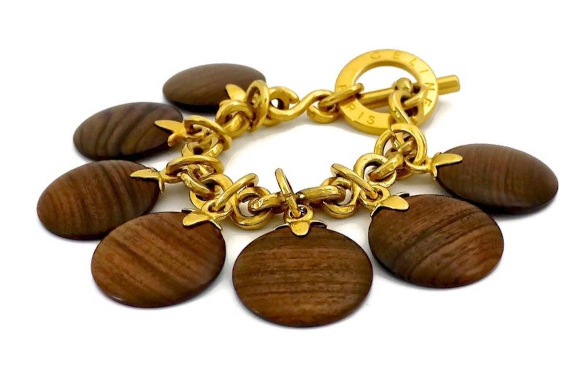 Vintage CELINE PARIS Medallion Wood Charm Bracelet

Measurements:
Height: 2.16 inches (5.5 cm)
Wood Charm: 1.38 inches (5.5 cm)
Length: 8.66 inches (22 cms)

Features:
- 100% Authentic CELINE PARIS.
- 7 medallion wood charms.
- Gold tone.
- Toggle