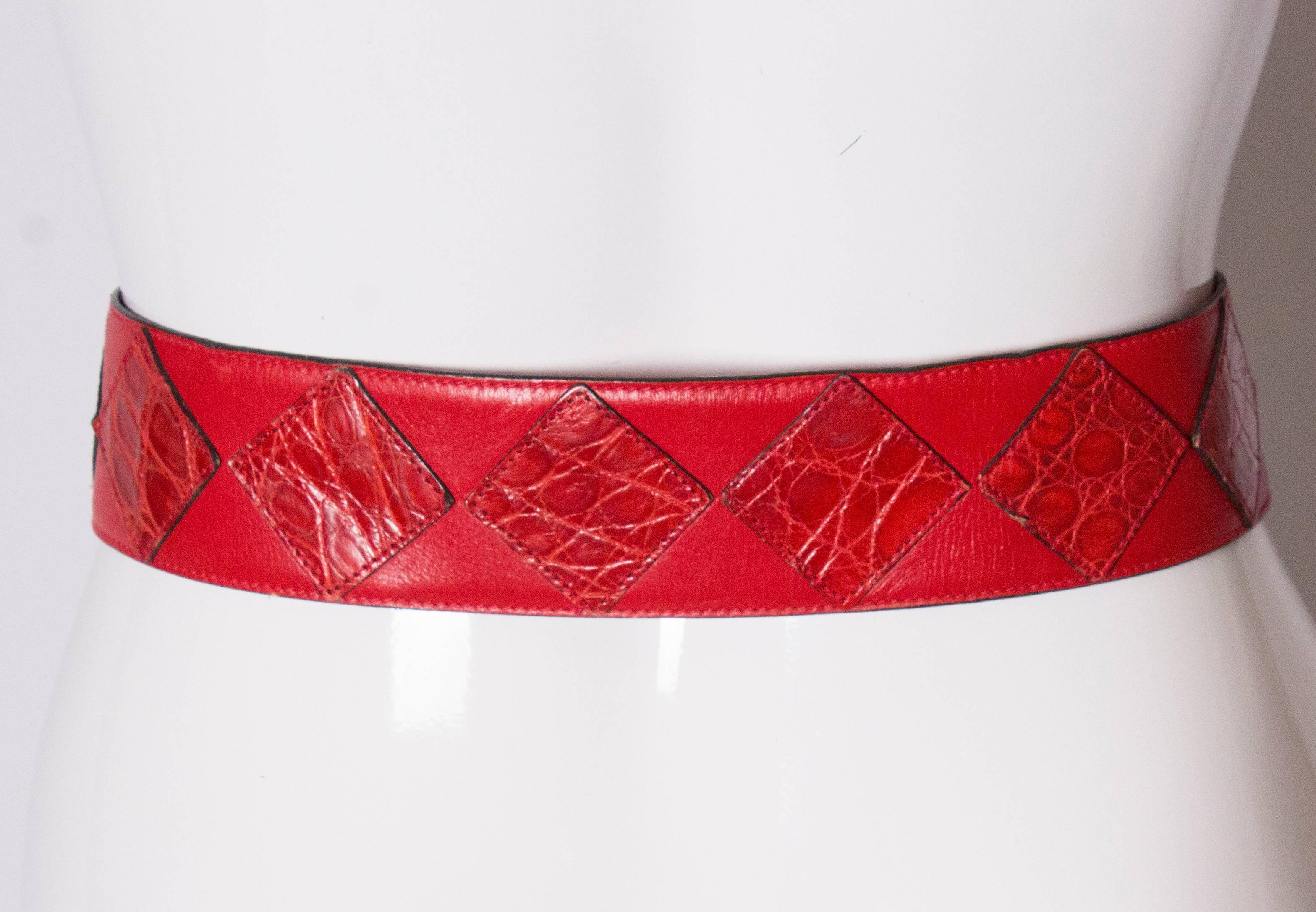 A chic belt by Celine. The belt is made of red leather, with red snakeskin decoration. It has a large 'gold' buckle stamped Celine, and 3 holes in the leather.