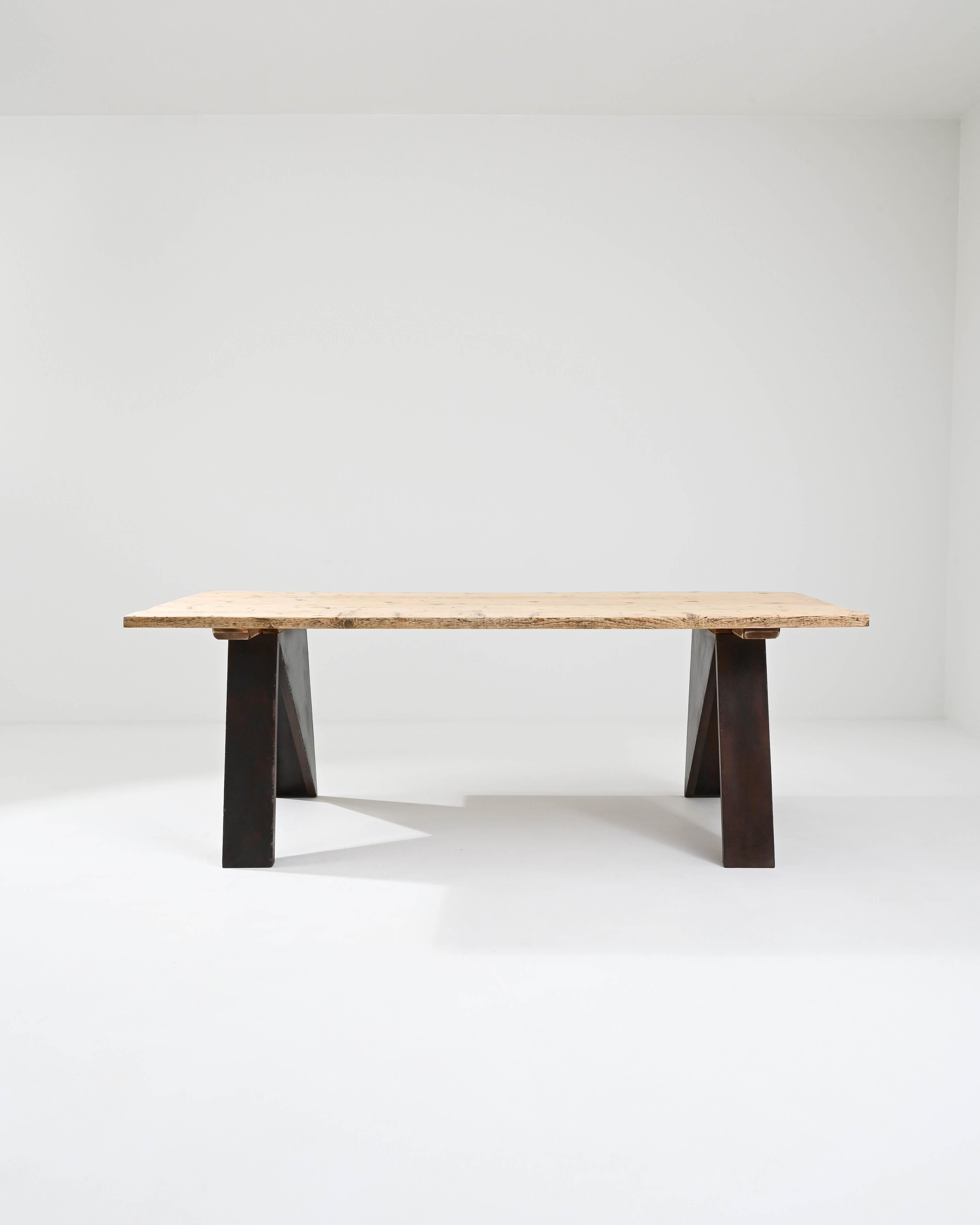 A metal dining table with a wooden top made in 20th century central Europe. This one of a kind prototype is composed with a vintage top supported by a metal base constructed in our atelier. Thick plates of steel have been welded together in a