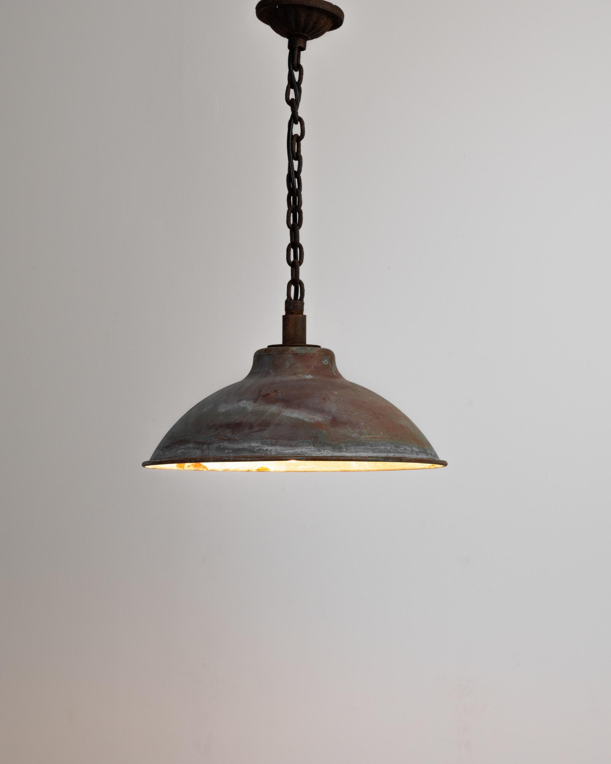 A copper plated industrial lamp from Central Europe, produced during the 20th Century. After descending two feet from the ceiling down an iron chain and canopy, colors whorl across the face of this lamp like storms across Jupiter. Shining bright,