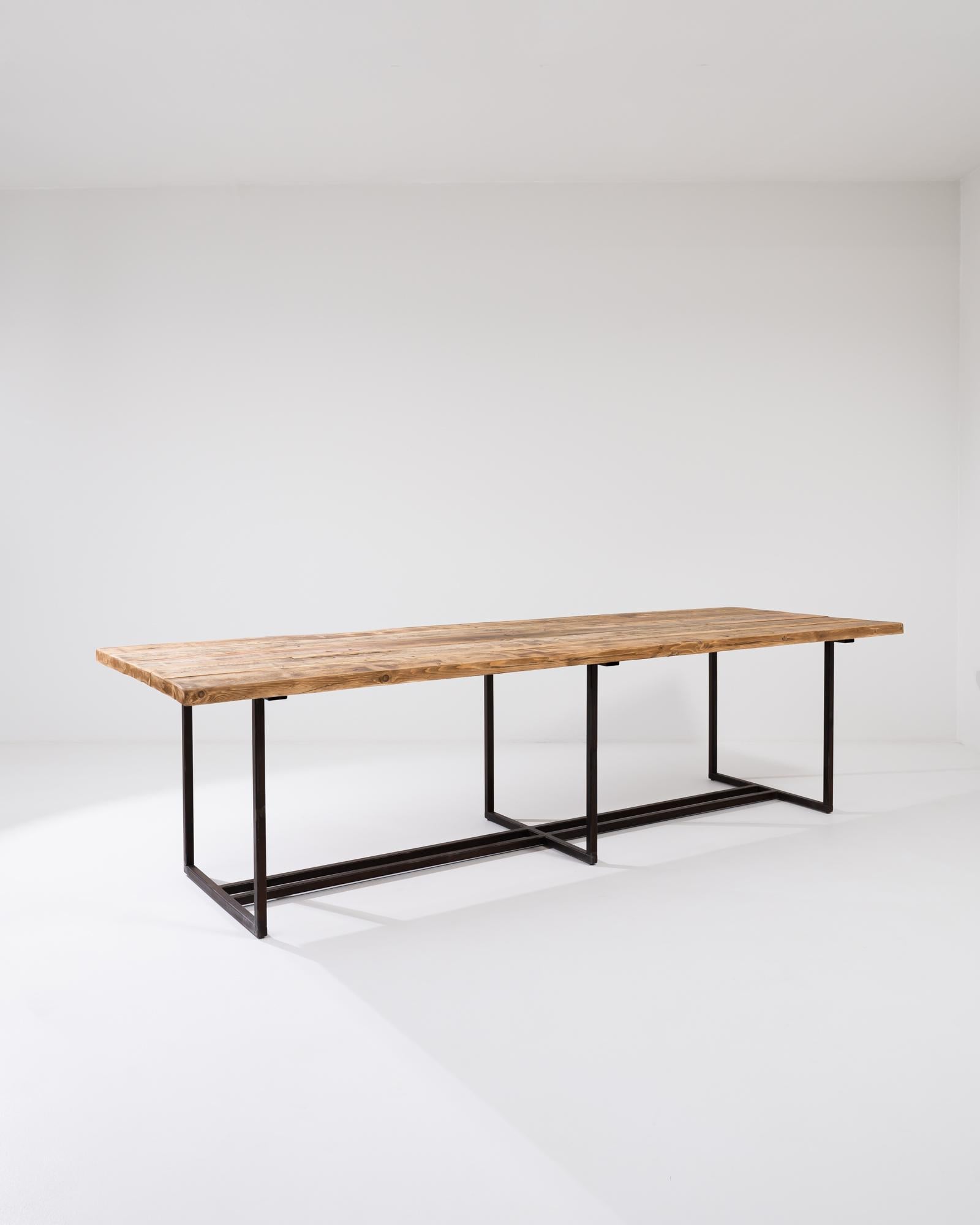 A metal dining table with a vintage wooden top from Central Europe. The time worn wooden top has been outfitted with a minimal metal base in our atelier. The geometric structure is composed with interlocking pairs of legs, the timeless design