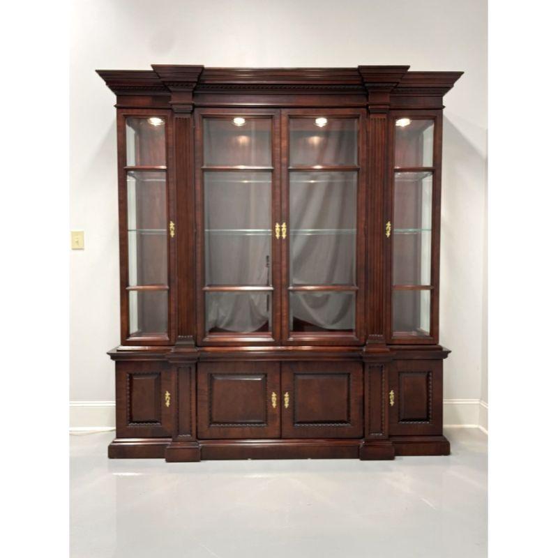 A Traditional style breakfront china cabinet by Century Furniture. Mahogany with brass hardware, crown molding at top, carved fluted columns, column caps and decorative carving to lower cabinet doors and columns base. Upper lighted cabinet has three