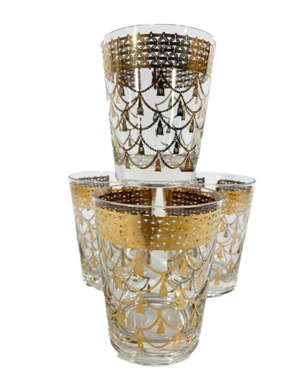 Four rare Mid-Century Modern double old fashioned glasses by Cera Glassware decorated in 22 karat gold with tasseled cords hanging from an openwork band with a gap and what appears to be a clasp, perhaps meant to depict a necklace.