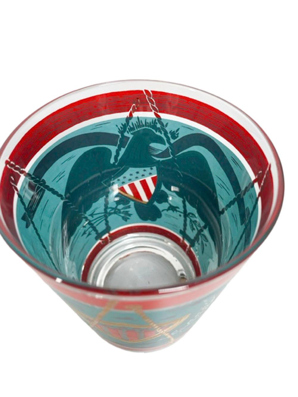 Mid-Century Modern rocks or double old fashioned glasses by Cera Glass decorated as a patriotic drum in teal and red enamel with a 22 karat gold eagle with a stars and stripes shield below a banner with the motto E Pluribus Unum.