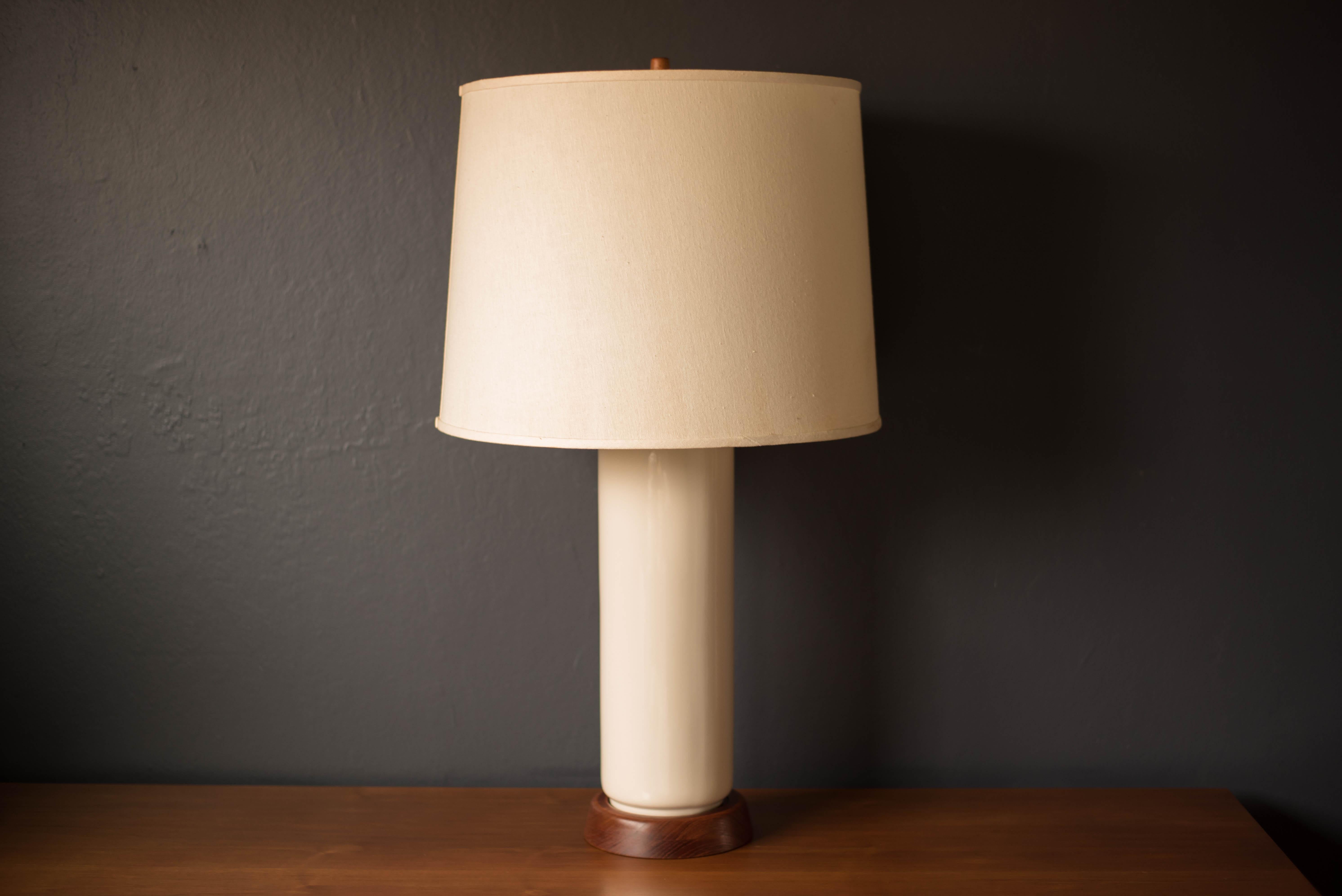 Mid Century Modern white cylinder table lamp, circa 1950s. This sculptural piece is accented with a walnut base and finial. Includes the original milk glass diffuser, brass socket, and drum shade. Functions with a three-way switch.