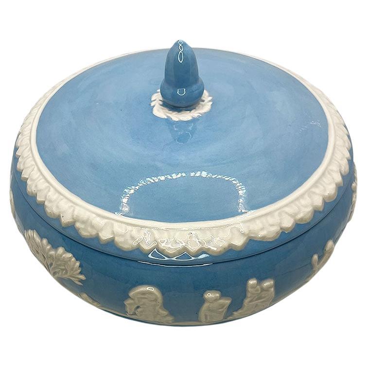 Plato redondo de cerámica de color azul bebé brillante con tapa. Esta pieza es redonda y presenta una escena figurativa mediterránea en blanco sobre un brillante fondo esmaltado azul bebé. La tapa cubierta es del mismo color azul, con una estilizada