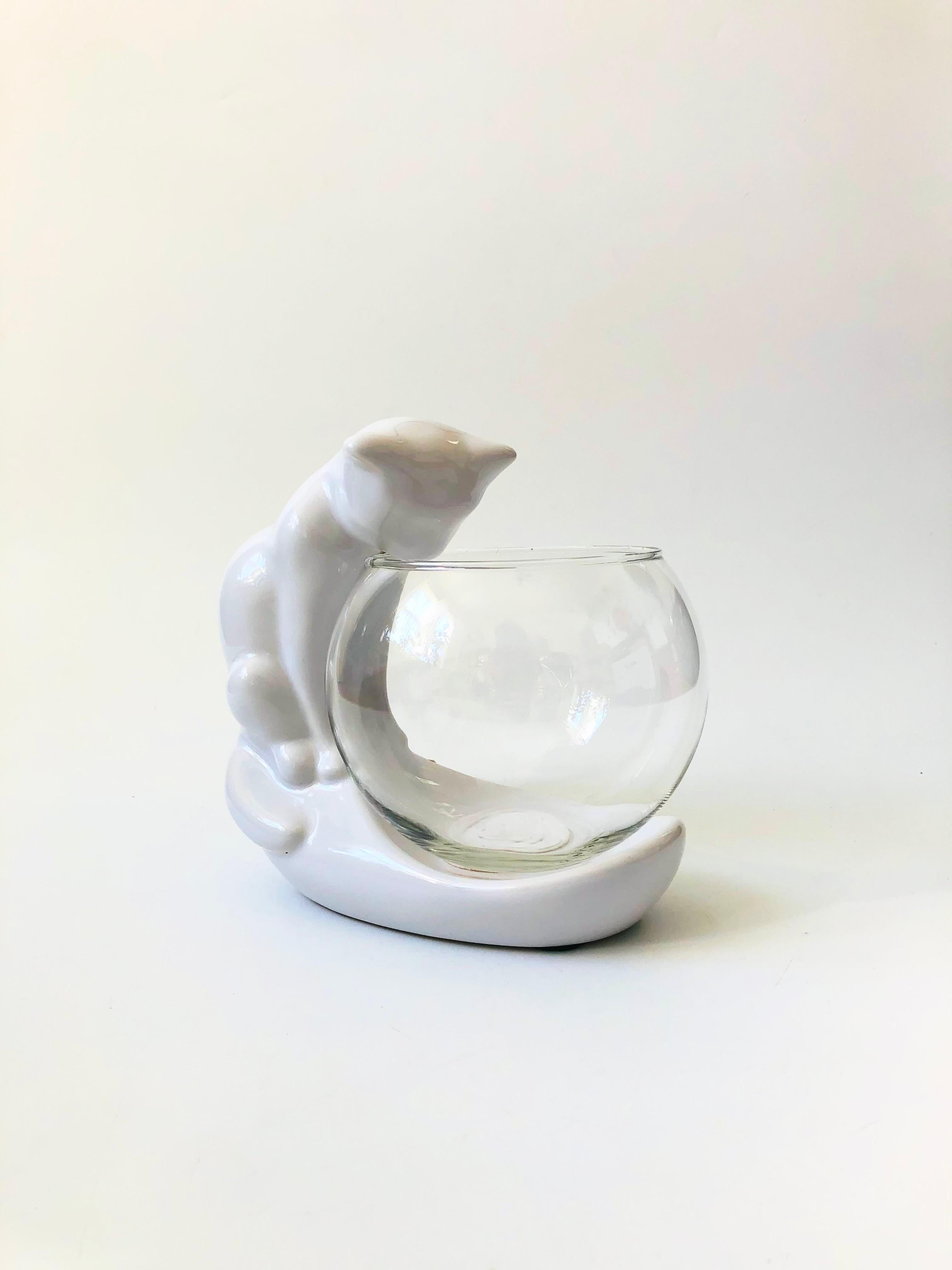 A wonderful vintage cat fishbowl from the 1980s. The fishbowl stand is made of glossy white ceramic in the shape of a cat peering down into the bowl. The glass bowl would be perfect for keeping a small fish or using as a terrarium. Made by Haeger