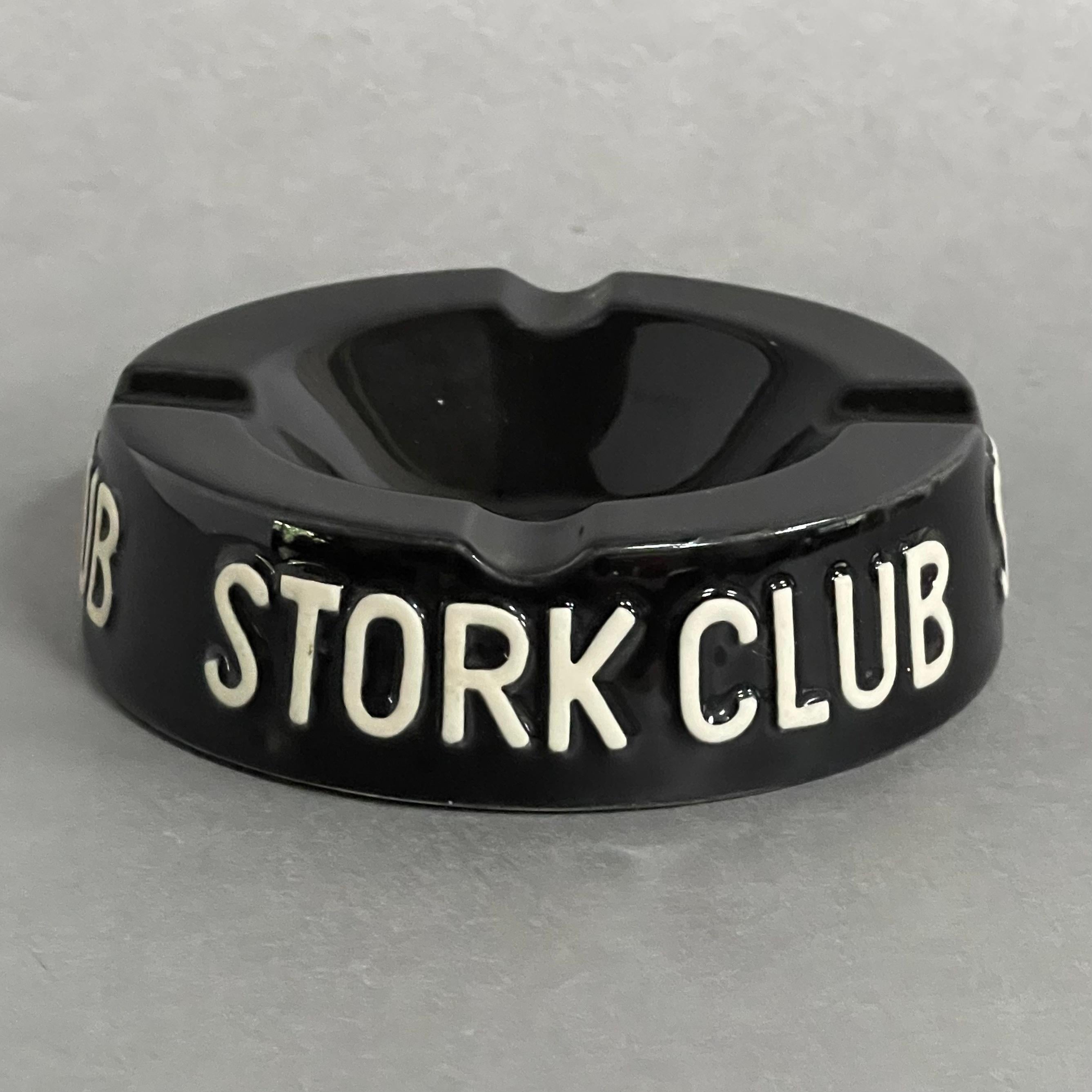 This terrific piece harkens to the heyday of nightclubs filled with jazz music and dense smoke. This round ceramic ashtray is glazed a dark piano black with raised white letters of the Stork Club.

The Stork Club, the iconic night spot on 3 East