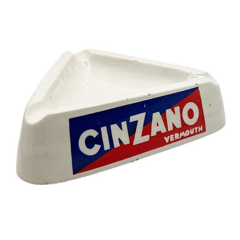 A vintage CinZano vermouth ashtray or catchall. This dish is triangular in shape and created from crisp white ceramic. There are three sides, and each side is labeled with CinZano Vermouth logo on a blue and red background. The bottom is stamped in