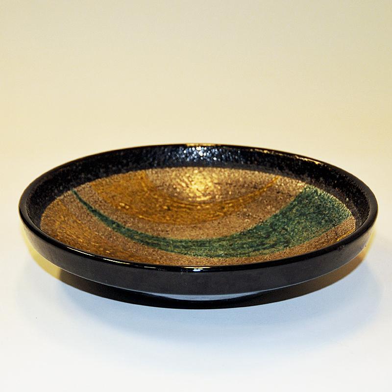 Vintage ceramic bowl 'Campo' in rough and glazed ceramic by Ingrid Atterberg for Upsala Ekeby in the 1960s. Yellow and blue/green claw shaped decor in the middle of the bowl. Beige brown base color and dark brown edge and back side color. Sweden,