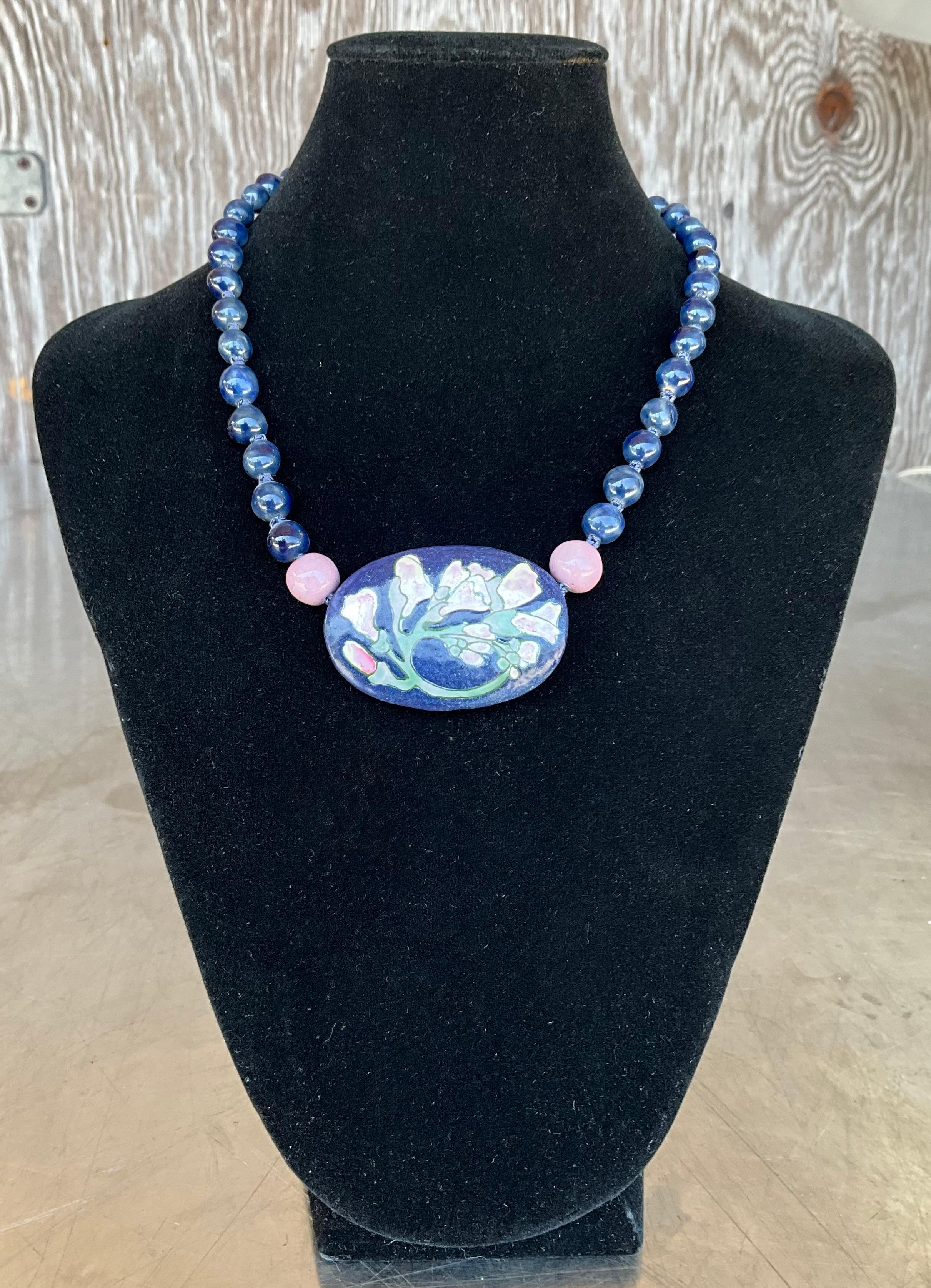 Questa collana di fiori in ceramica vintage con perline di sodalite è un'affascinante miscela di arte artigianale ed eleganza naturale. Al centro della collana si trova un ciondolo a forma di fiore in ceramica splendidamente dettagliato,