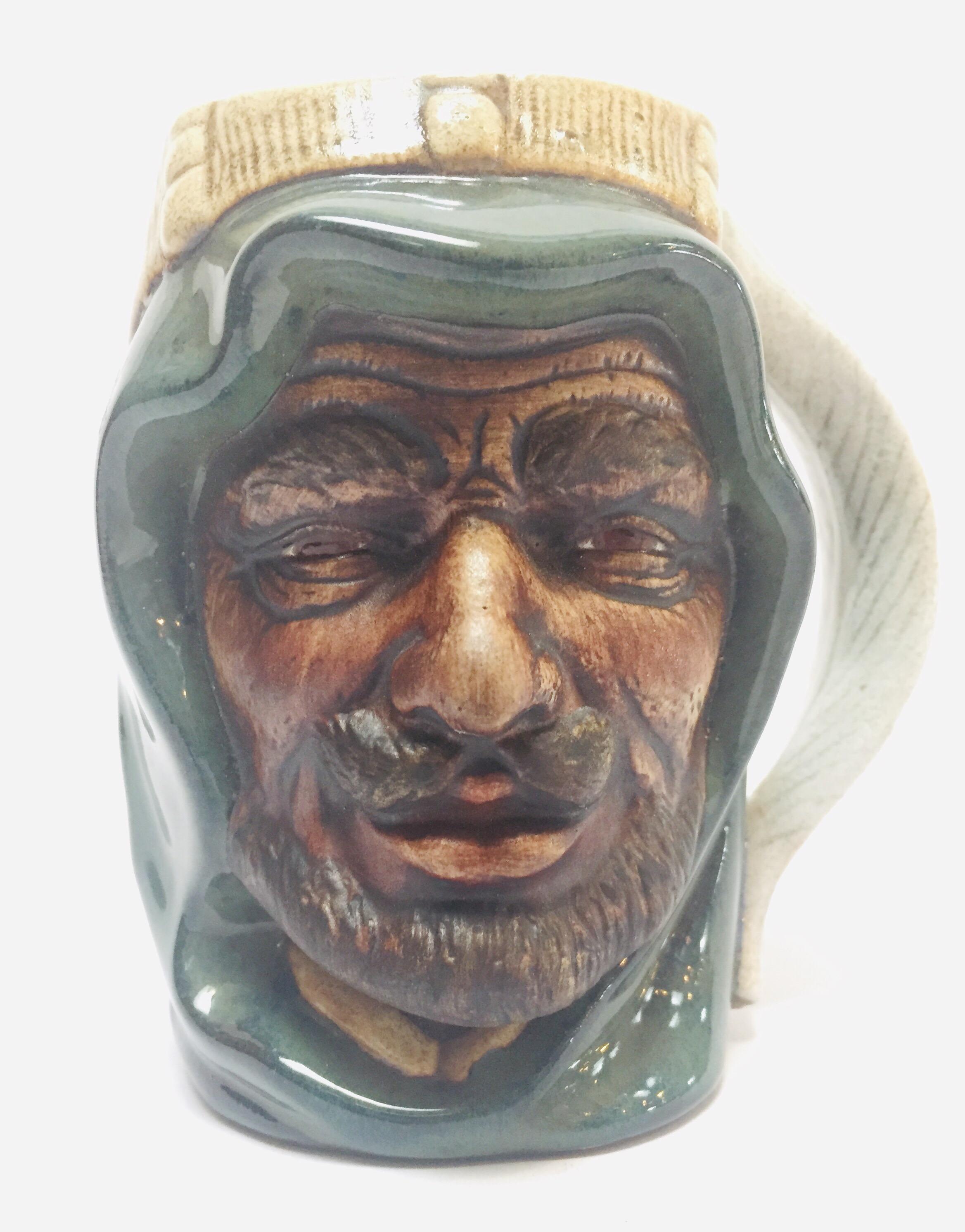 Vintage molded ceramic Middle Eastern Moorish Arab man character Toby mug.
Hand painted molded glazed ceramic cup shaped like the head of a bearded Moorish man with dark skin wearing keffiyeh (headdress) with a feather-shaped handle on one side.