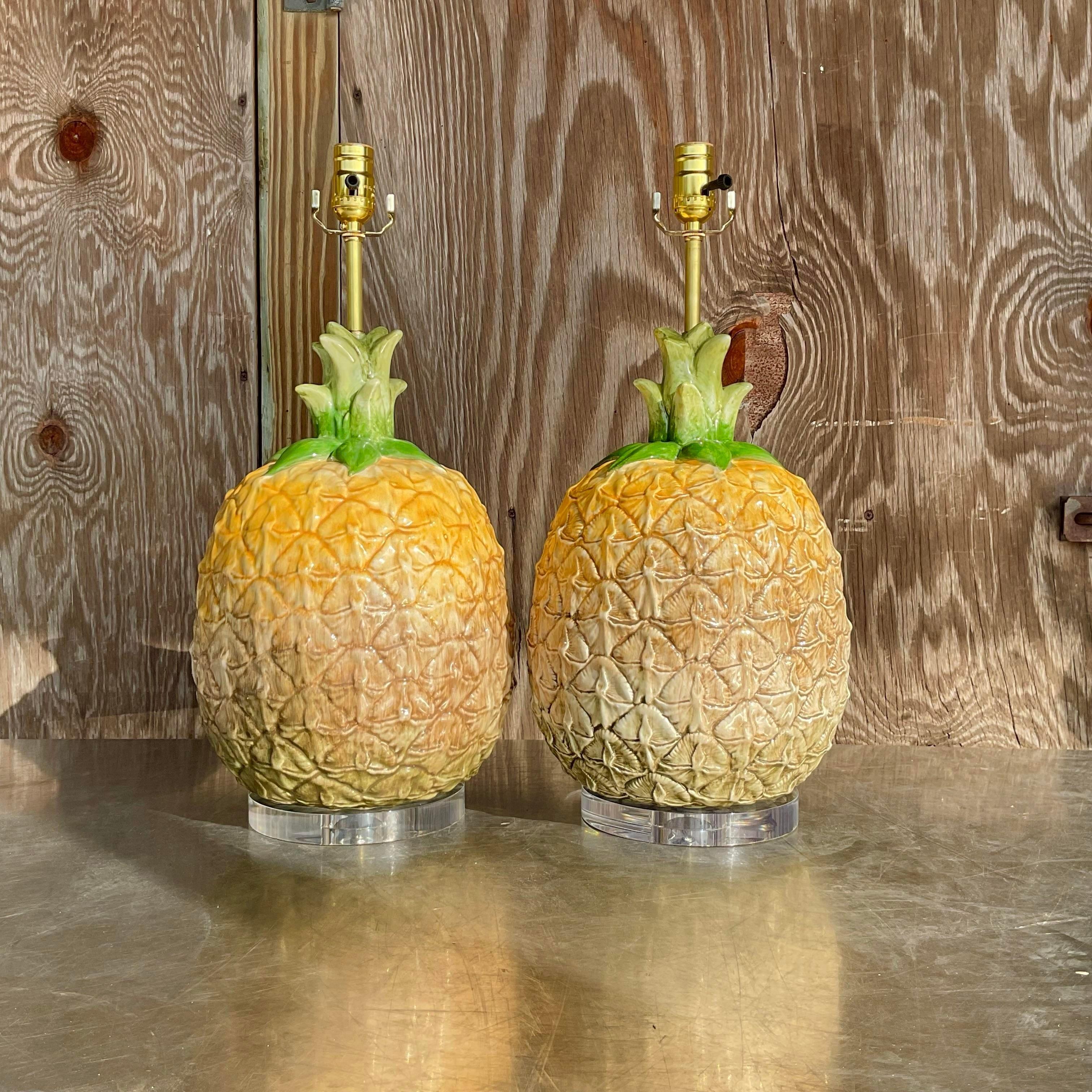 Epic vintage pair of ceramic pineapple lamps. Hand made and hand painted then adhered to a modern lucite base with brass neck and socket. Immediately add a sense of whimsy and playfulness to any coastal space. These lamps are able to maintain a
