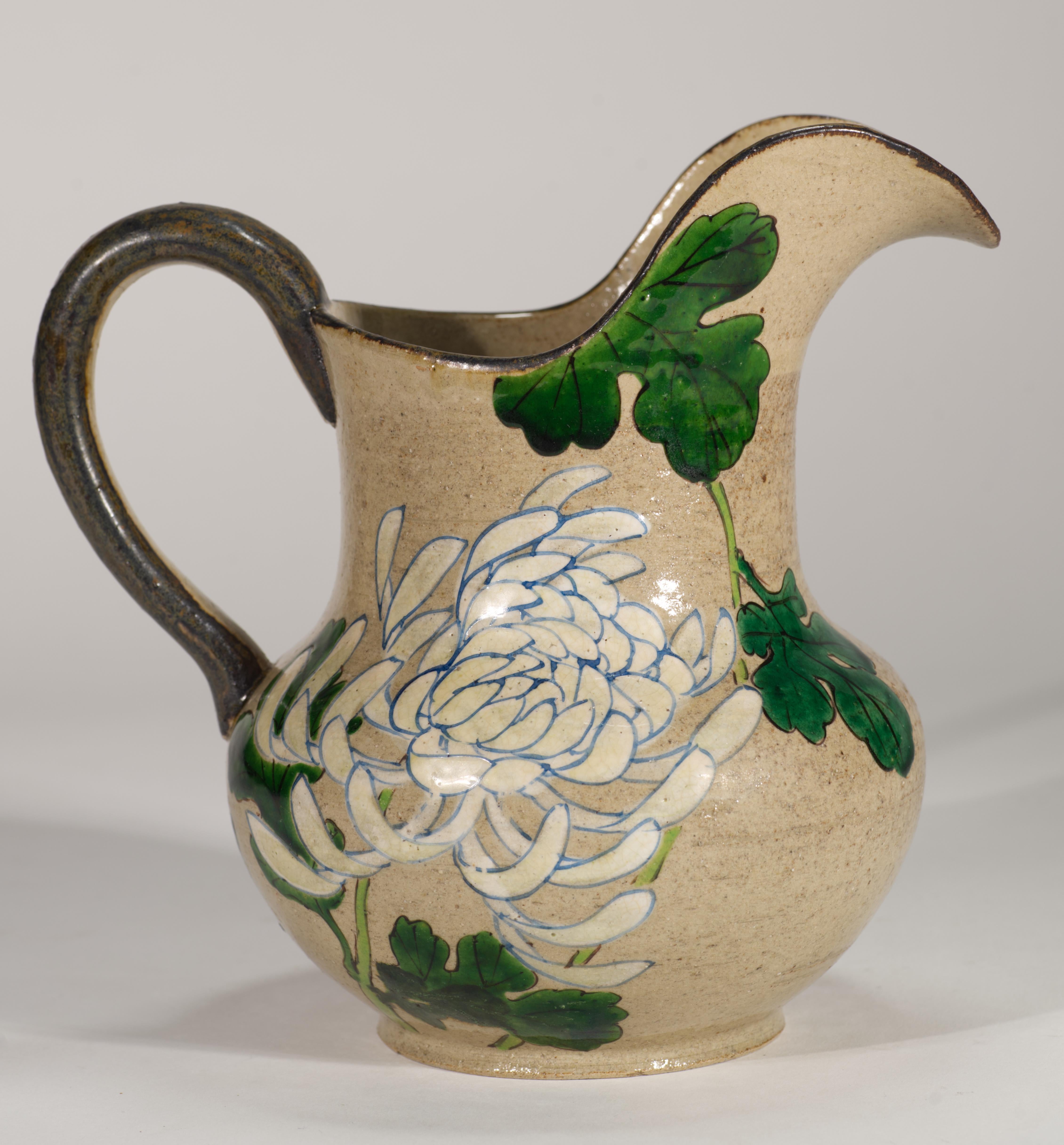  Il vaso vintage a forma di brocca presenta decorazioni floreali stilizzate in grande scala su entrambi i lati del vaso. Fiori e foglie di crisantemo dai contorni contrastanti sono dipinti a mano con uno smalto leggermente in rilievo sullo sfondo di