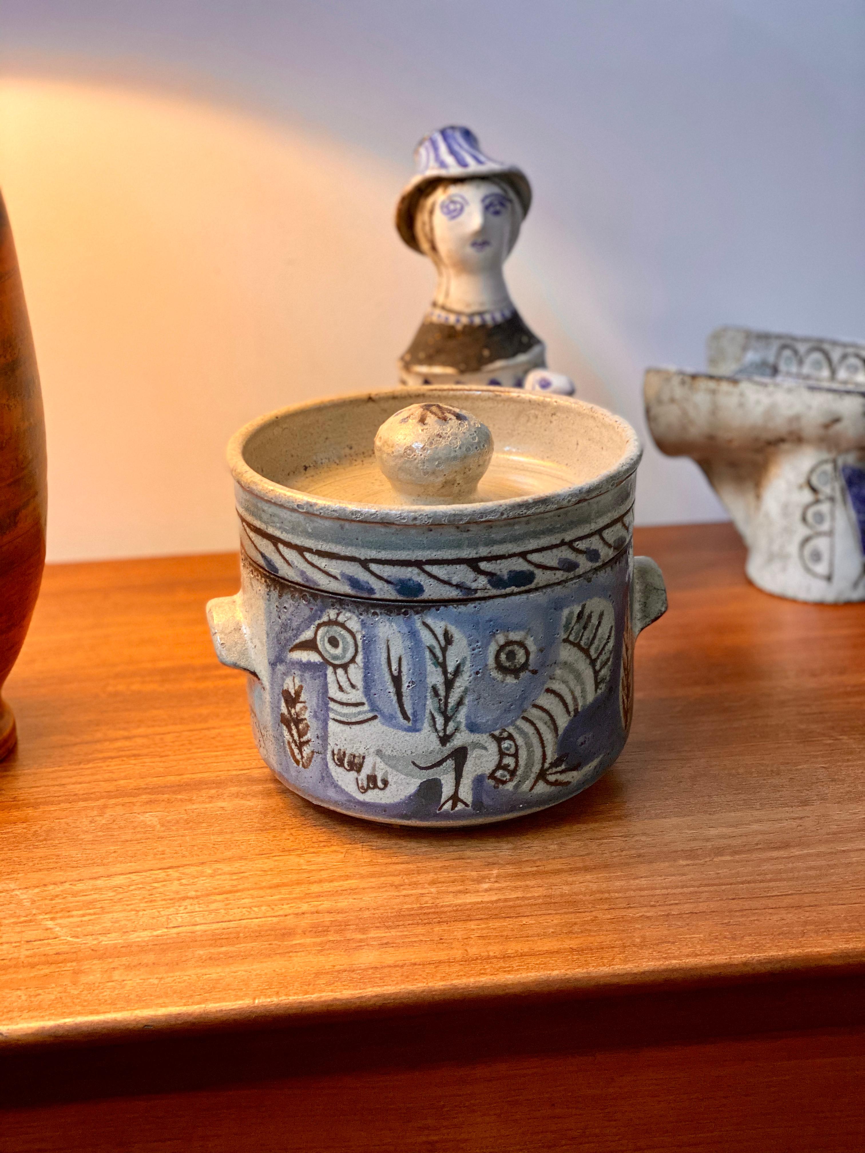 Decorative vintage ceramic pot with lid by Gustave Reynaud, Le Mûrier (circa 1950s). This utilitarian crockery pot with lid is also a stunning work of art. On the rustic exterior is a stylised, off-white peacock with plant motifs framed in Reynaud's