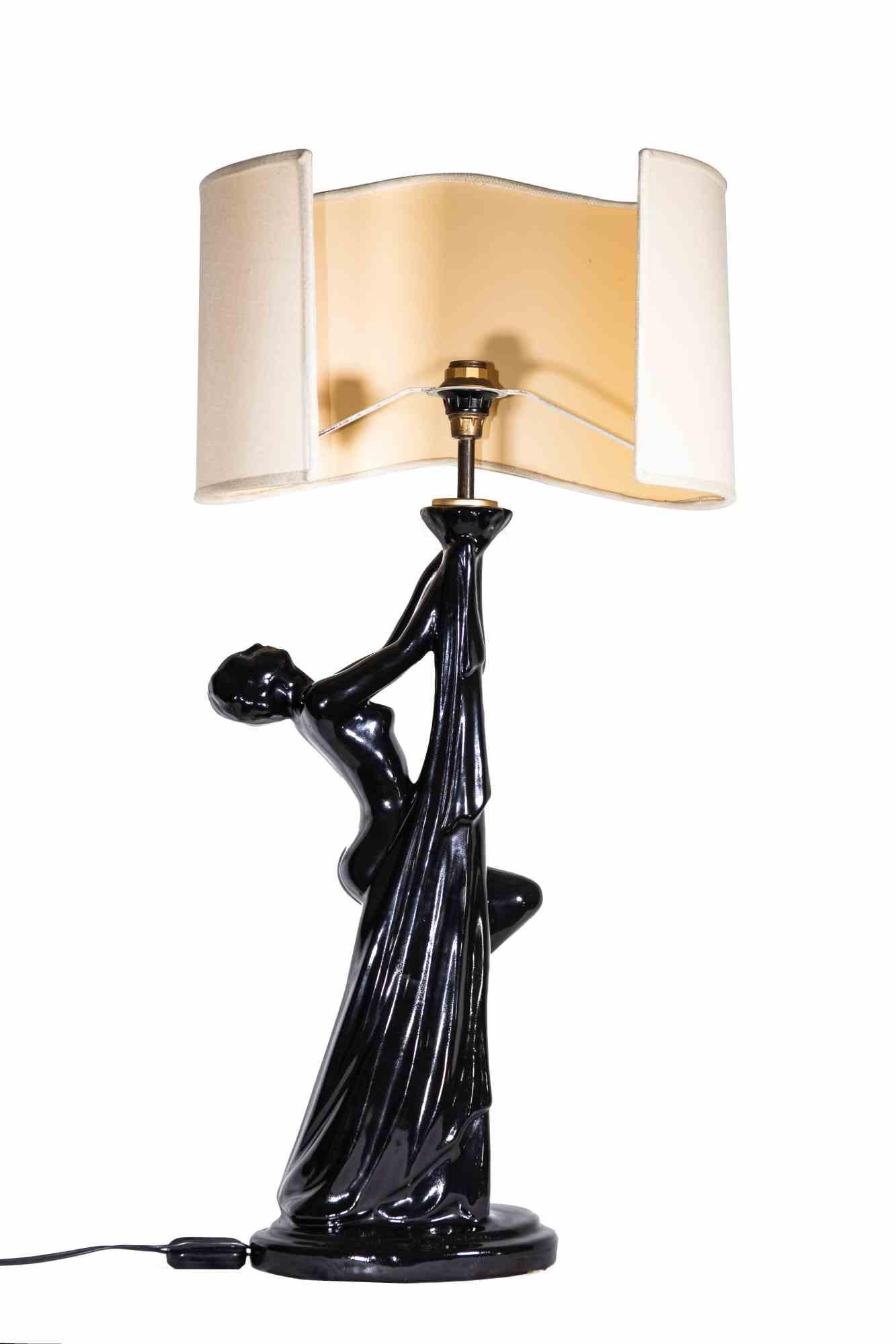 La lampada da tavolo Woman è una lampada dal design originale realizzata da Tommaso Barbi negli anni Settanta. 

Una lampada unica con una struttura in ceramica nera a forma di donna e un paralume in tessuto dalla forma sinuosa.
    