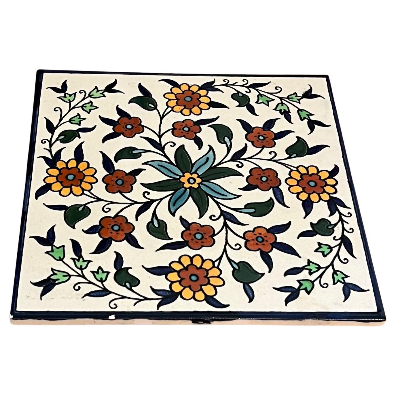 Piastrella di ceramica d'epoca raffigurante un disegno floreale dipinto a mano.