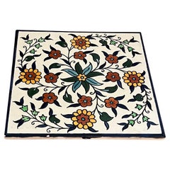Vintage-Keramikfliese, die ein handgemaltes Blumendesign darstellt.