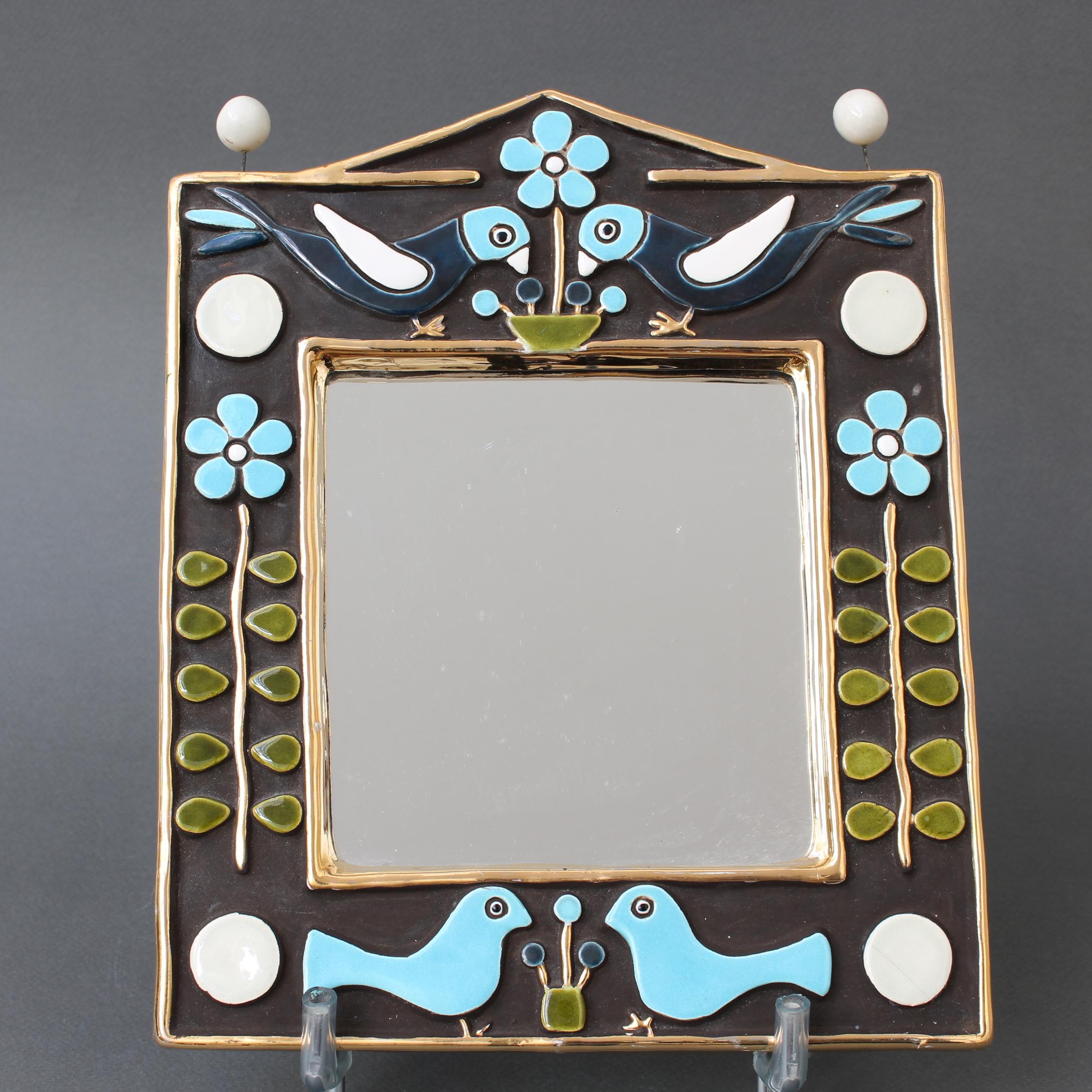 Ceramic wall mirror with birds and flowers (circa 1970s) by Mithé Espelt. A delightful decorative piece topped with two pairs of whimsical enamel birds above and below the square mirror. The mirror is framed with a gold crackle glaze which also