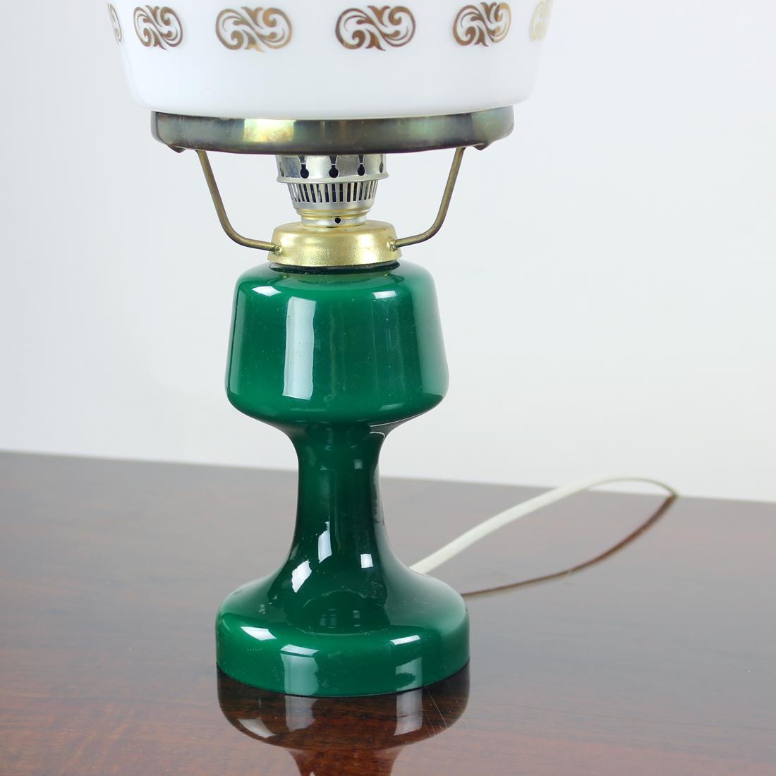 Beautiful vintage table lamp. Produced by OPP Jihlava (Original label visible) in 1950s. The lamp has a green ceramic base which holds two glass shields. One in clear transparent glass and another one is in white opaline glass with gold ornaments.