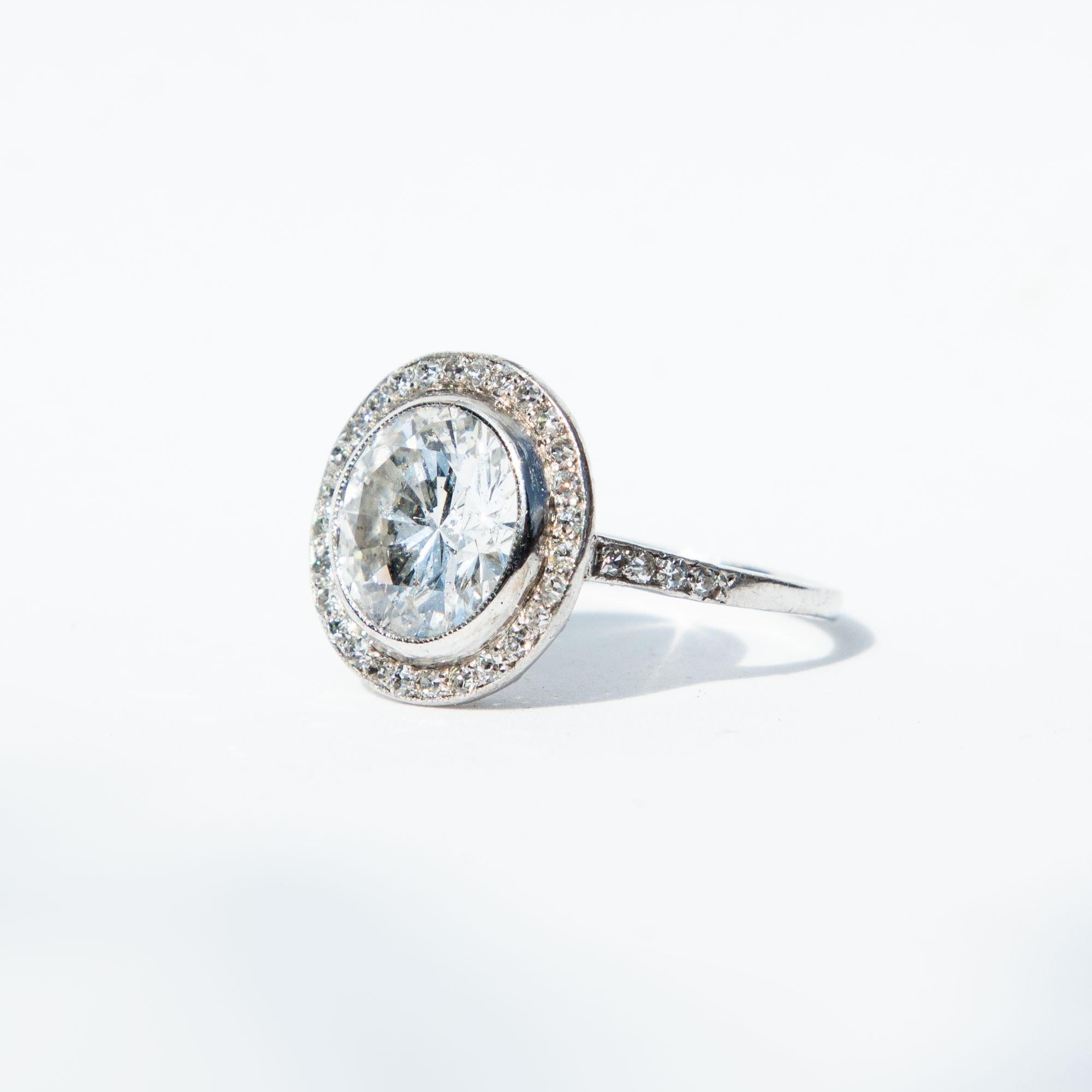 The stunning central diamond is a modern brilliant cut. This is surrounded by a halo of sparkling diamonds, with diamonds extending down the shoulders. Total diamond weight certified 3.62 carats, F colour and VS1/SI2 clarity. Modelled in platinum.