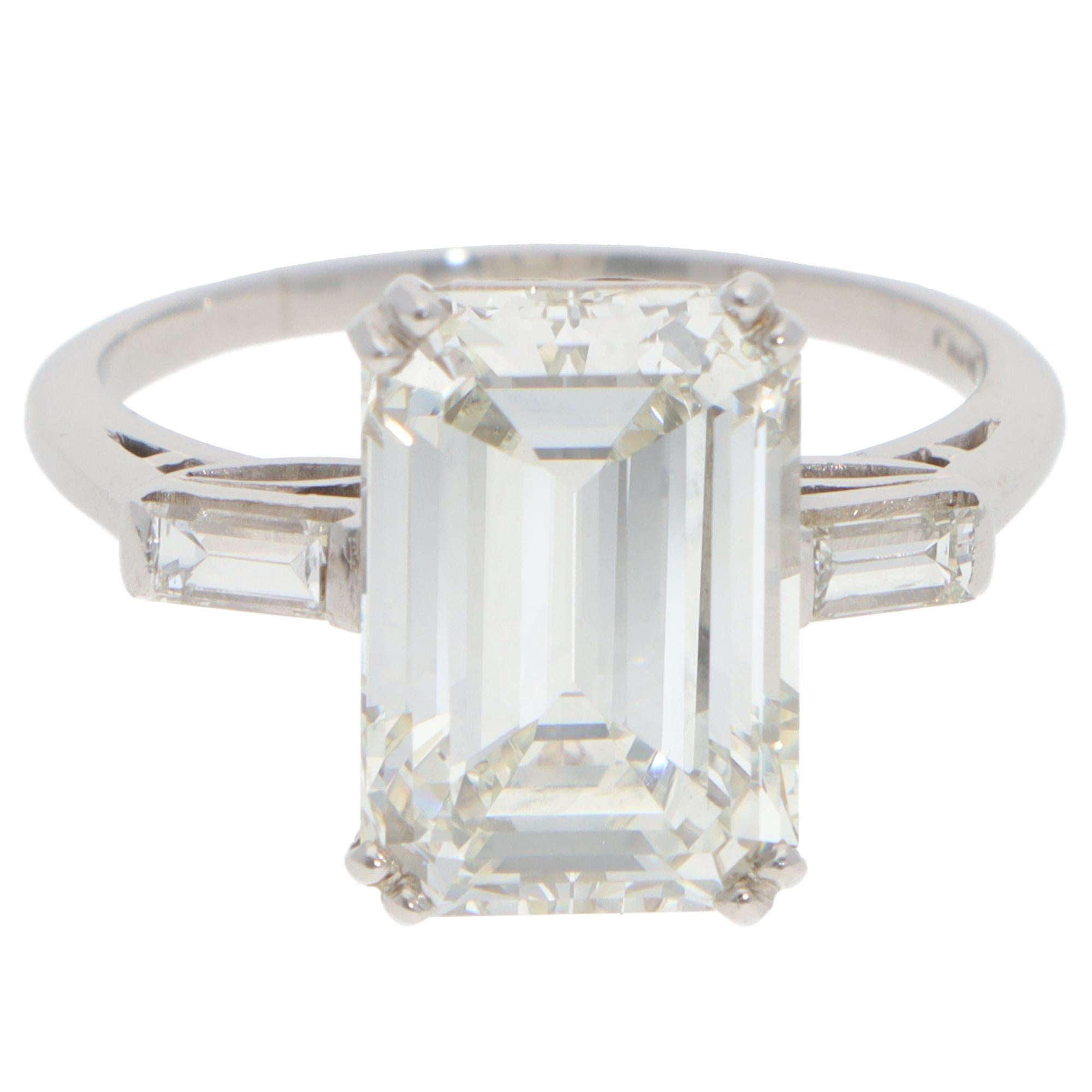 Une époustouflante bague vintage à trois pierres en diamant taille émeraude, sertie en platine.

La bague est ornée d'un diamant certifié de 6,35 carats de taille émeraude, serti sur deux anneaux, et de deux diamants de taille baguette sur le côté.