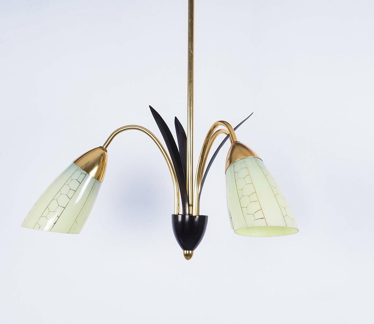 Brass chandelier with 3 green glass shades from the 1950s.

The lamp has 3 brass arms with 3 black metal leaves in between.

The opaline shades have a greenish yellow color with a fine honeycomb decor in gold.

Very elegant lamp due to the