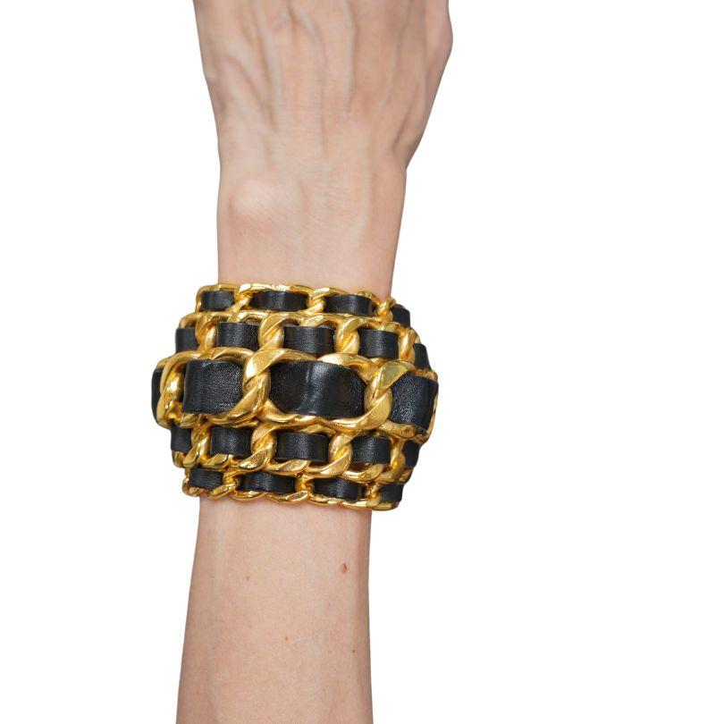 This vintage Chanel cuff bracelet from the Fall/Winter 1991 collection is a bold statement piece. It is crafted from interwoven gold-plated chain links and black leather, creating a distinctive layered design. The cuff has a diameter of 7 inches