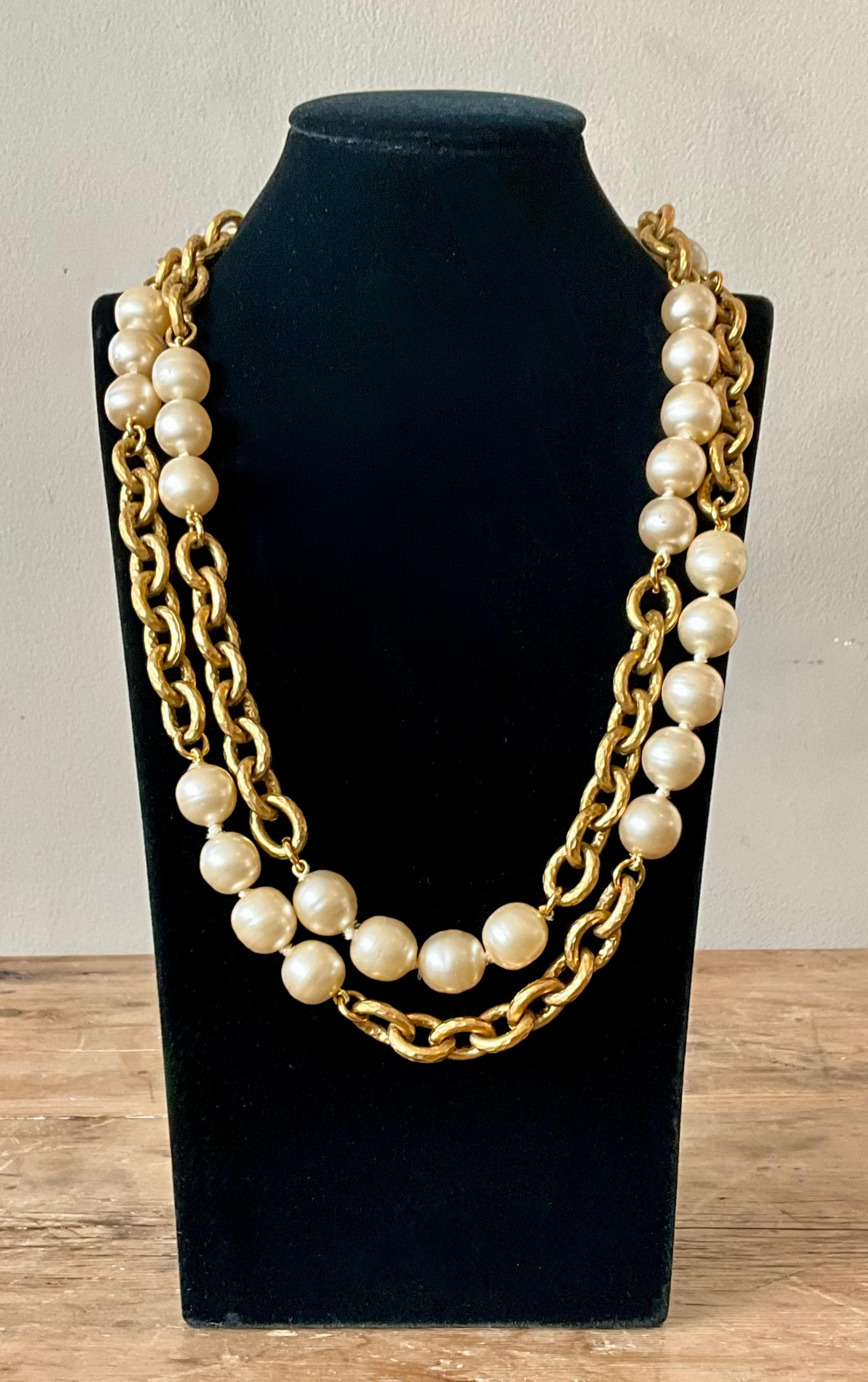 Questa collana vintage Chanel 1993 con catena di perle finte è un pezzo iconico che cattura l'eleganza e l'audacia del design classico di Chanel. Caratterizzata da finte perle lucenti accentuate da sostanziose catene dorate, questa collana incarna
