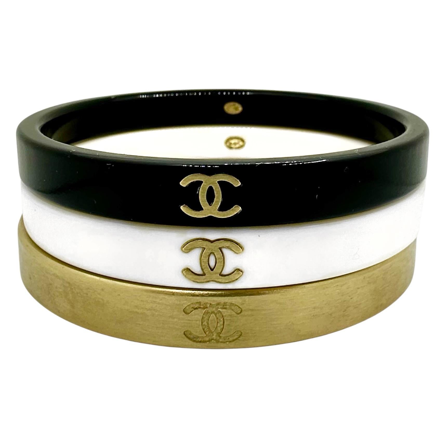 Este maravilloso conjunto vintage de Chanel se lanzó como parte de la colección Otoño 2010. El juego de tres brazaletes se compone de un brazalete de resina negra, un brazalete de resina blanca y un brazalete de metal cepillado en tono dorado. Cada
