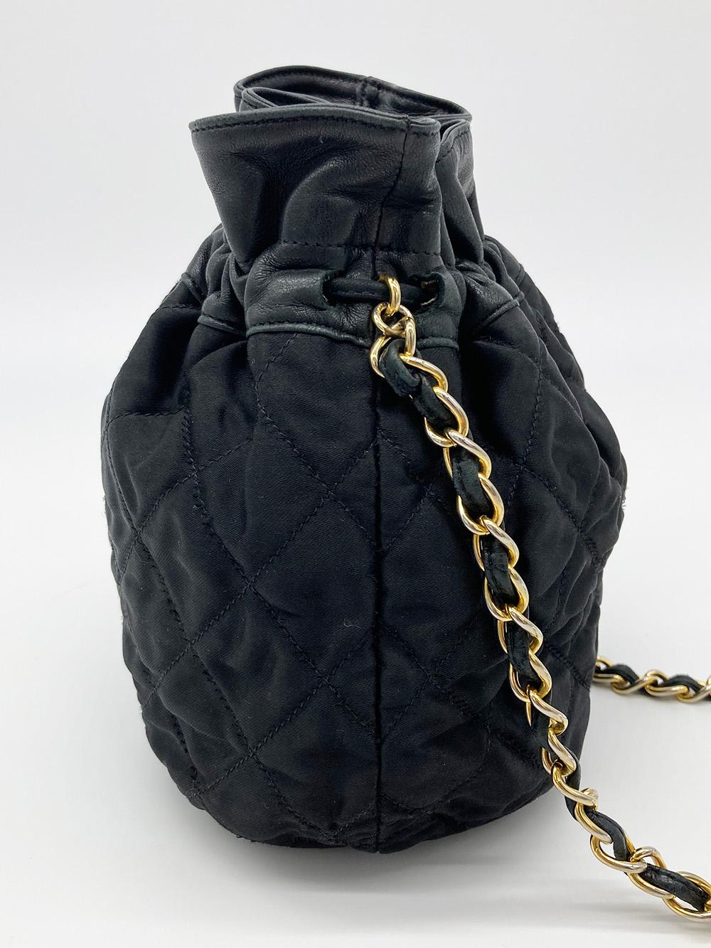 Vintage Chanel Black Satin & Leather Drawstring Bucket Bag in good condition. Black quilted satin exterior trimmed with black leather and a woven chain and leather shoulder strap. Quilted CC logo along bottom and small CC embossed button at end of