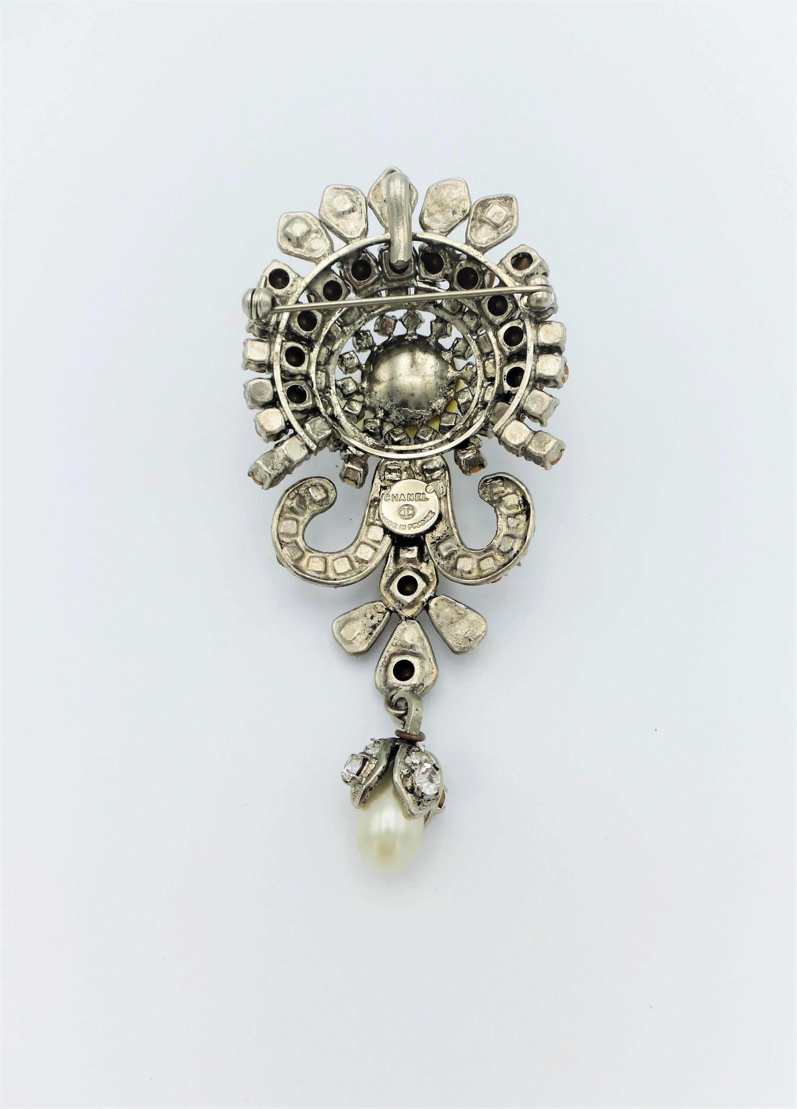 About
Very elegant Chanel brooch made of rhodium plated metal  and set with many rhinestones and 2 handcrafted beads.  A small moving pearl drop is attached.
Measurement: 
Length 9 cm (3,5 inches) 
Width    4 cm  (1,55 inches) 
High     2 cm  (1,8